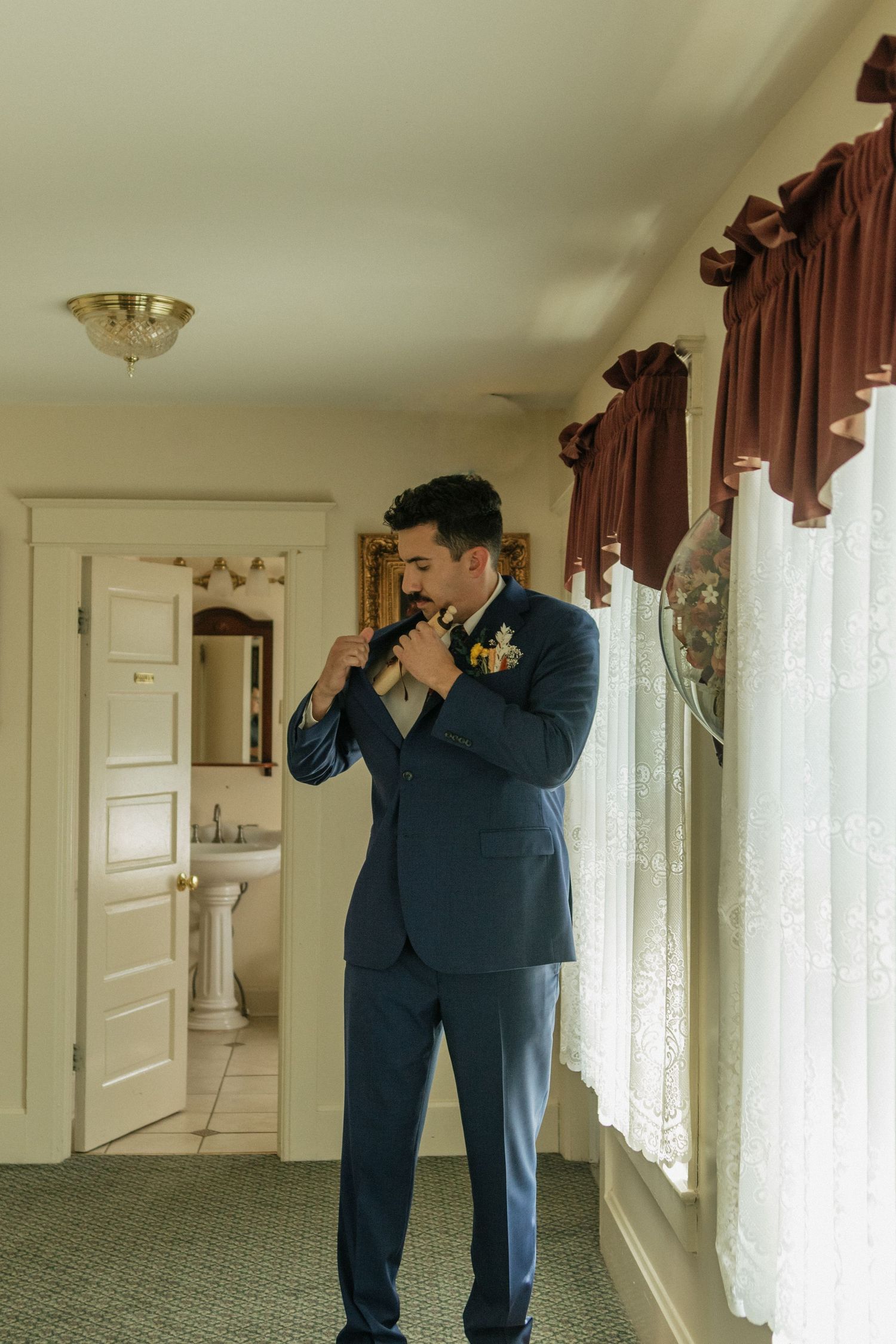 Groomsmen in navy suits prepare with emotional moments in a hotel hallway before the wedding ceremony.