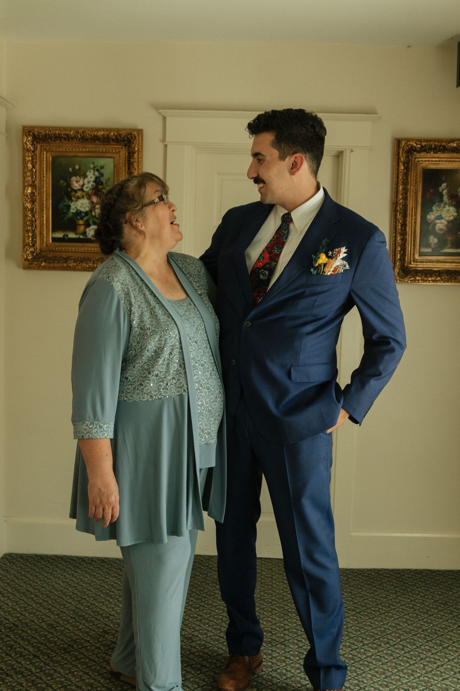 Two people share an emotional moment in formal attire during a wedding preparation.