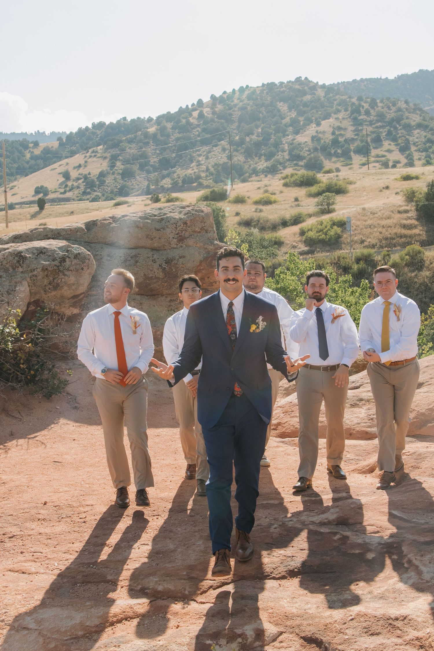 Groomsmen in navy and khaki suits posing together on rocky terrain with mountains in the background.