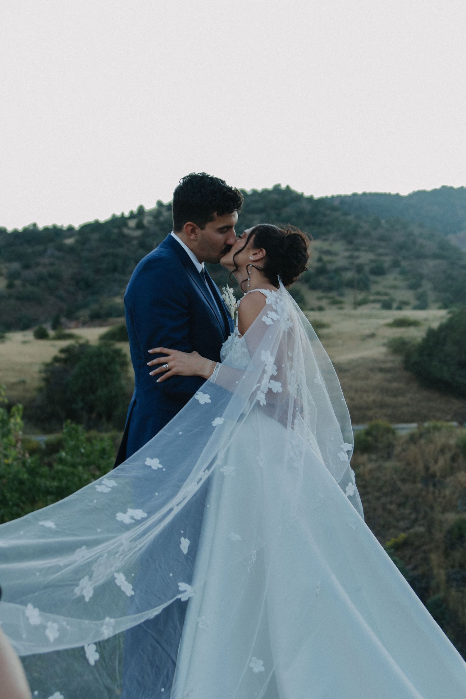 Couple in wedding attire share romantic moments against a mountainous backdrop.
