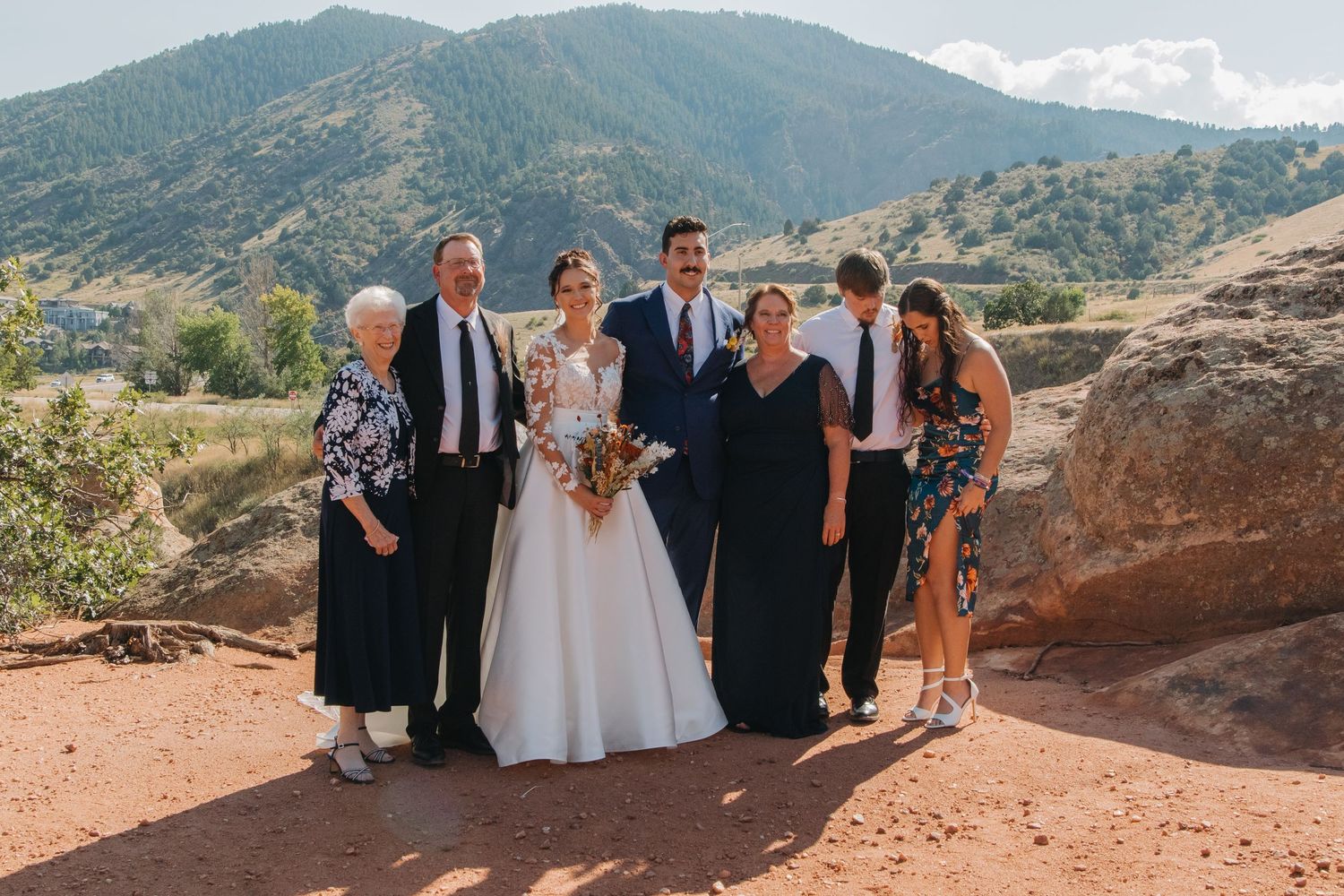 Wedding party gathered on red rocks with mountain landscape in background.