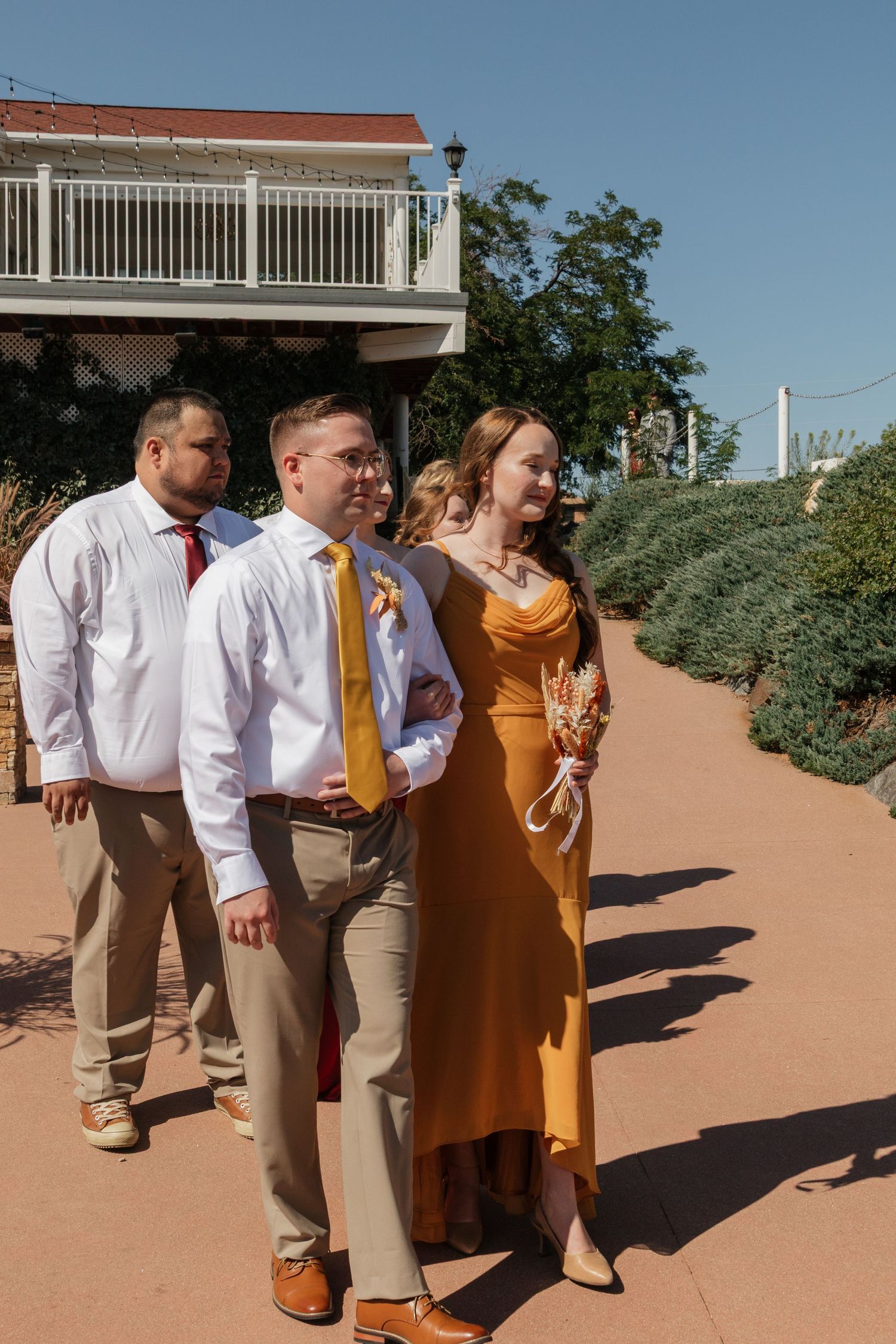 Wedding party members in white shirts and tan pants walk in line on a terracotta-colored path.