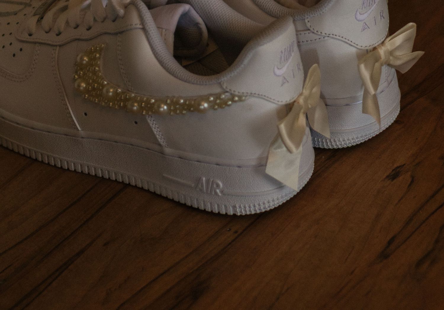 White sneakers with attached ribbon bows stand on wooden flooring with multiple angle views shown.