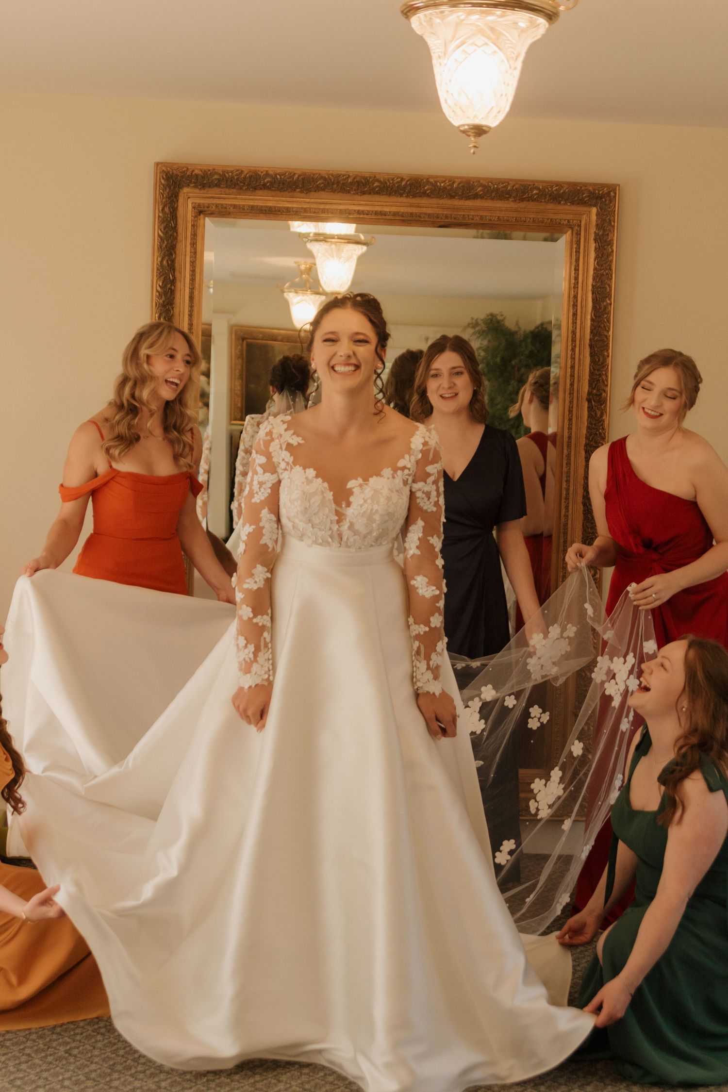Bridesmaids in colorful dresses gather around a wedding gown in excitement.