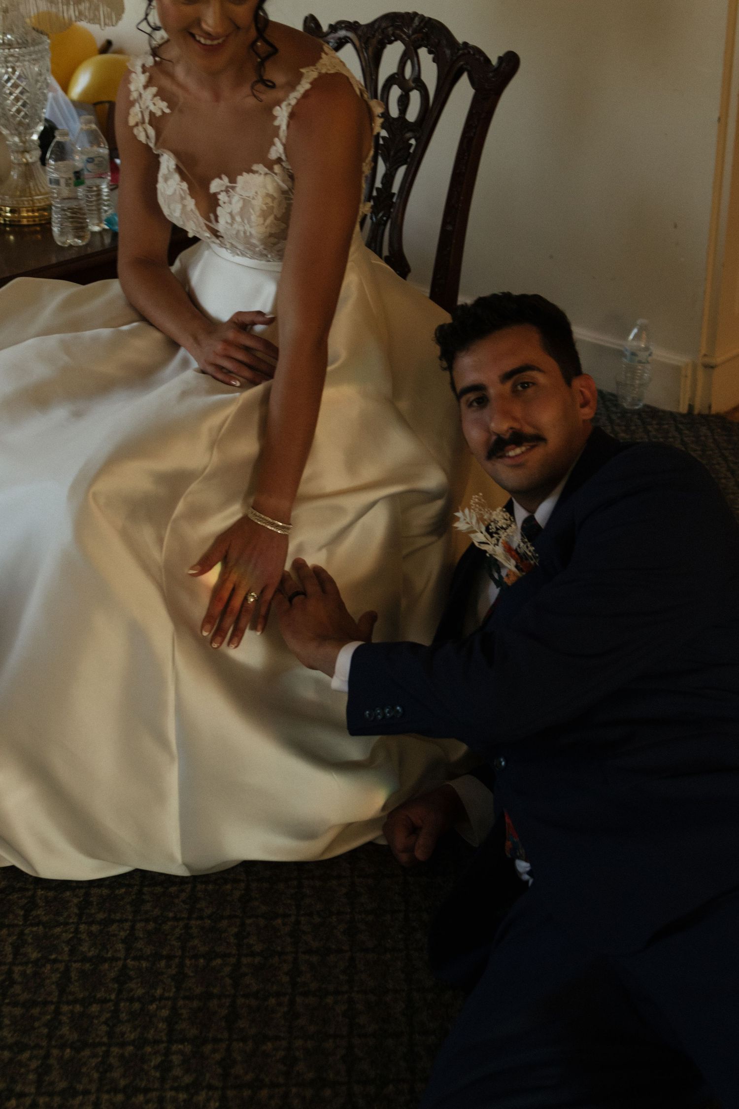 Wedding couple shares playful moment on carpeted floor during reception.