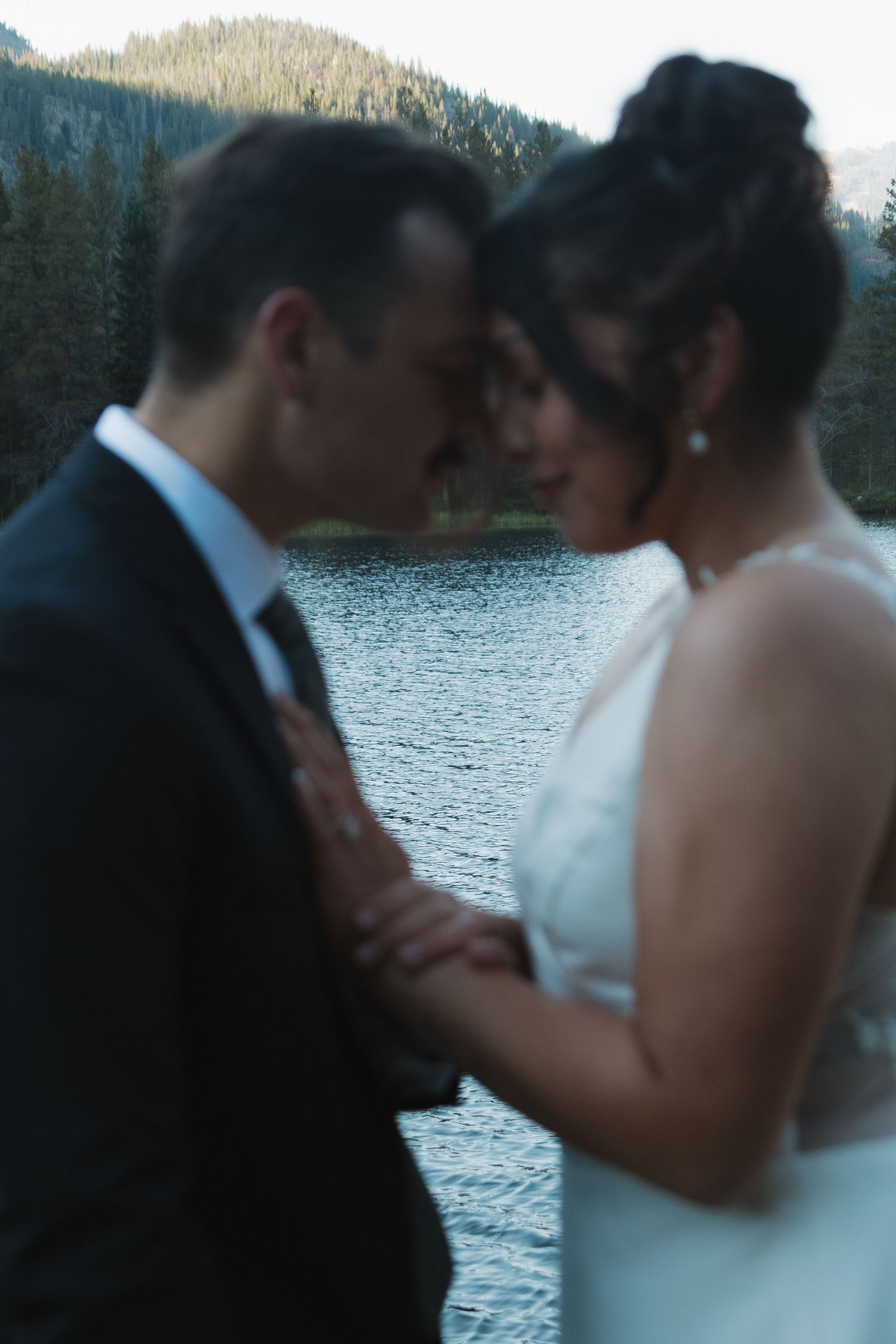 A couple shares a tender moment by a scenic mountain lake during their wedding celebration.