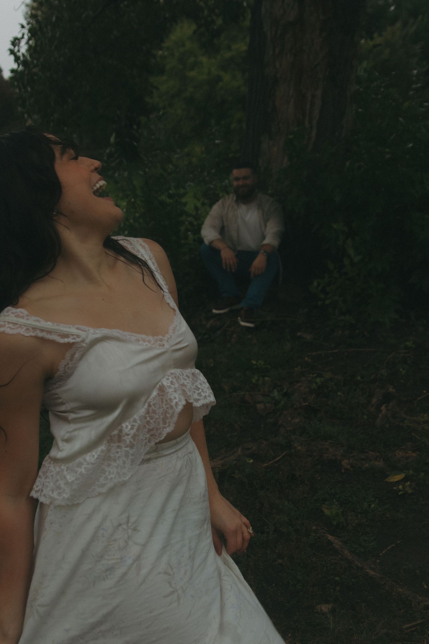 Person in white lace dress dances expressively against a dark wooded backdrop.