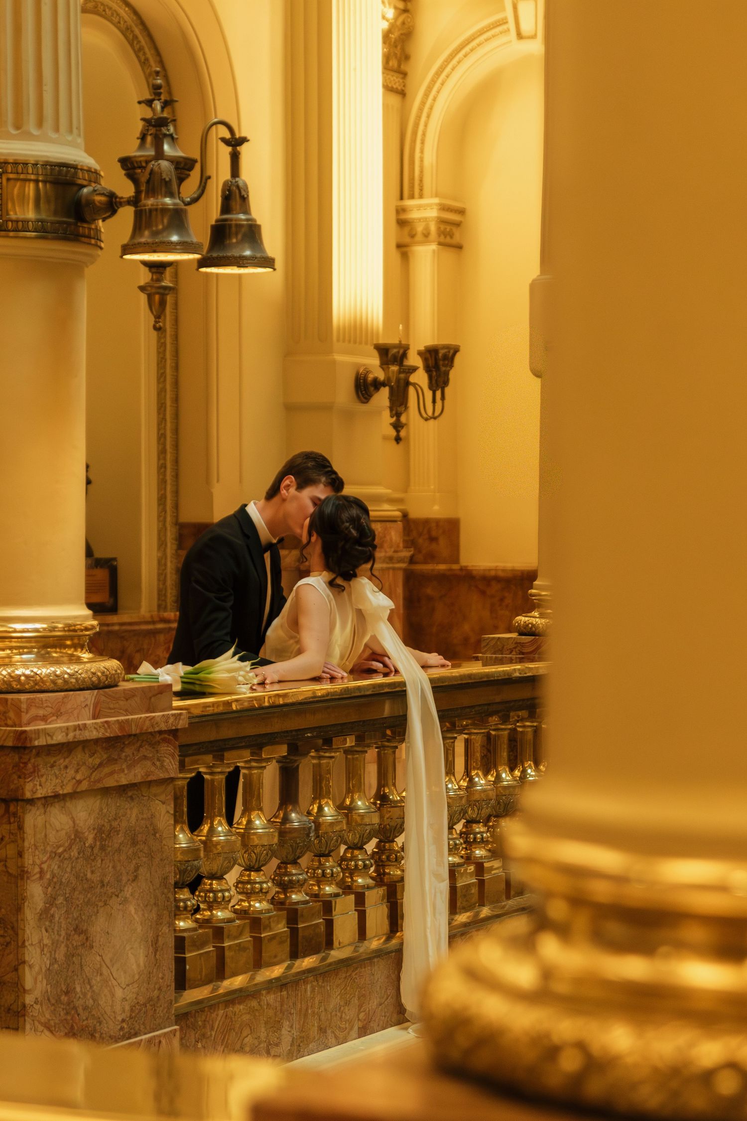 Couple sharing a romantic moment along an ornate marble balustrade in warm golden lighting.