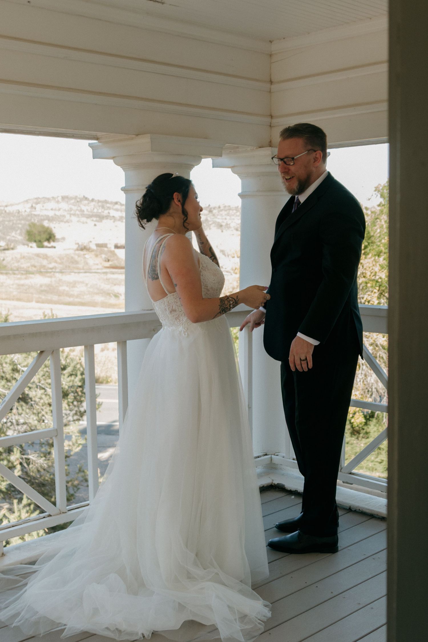 A couple shares an intimate first look moment on a white porch during their wedding day.