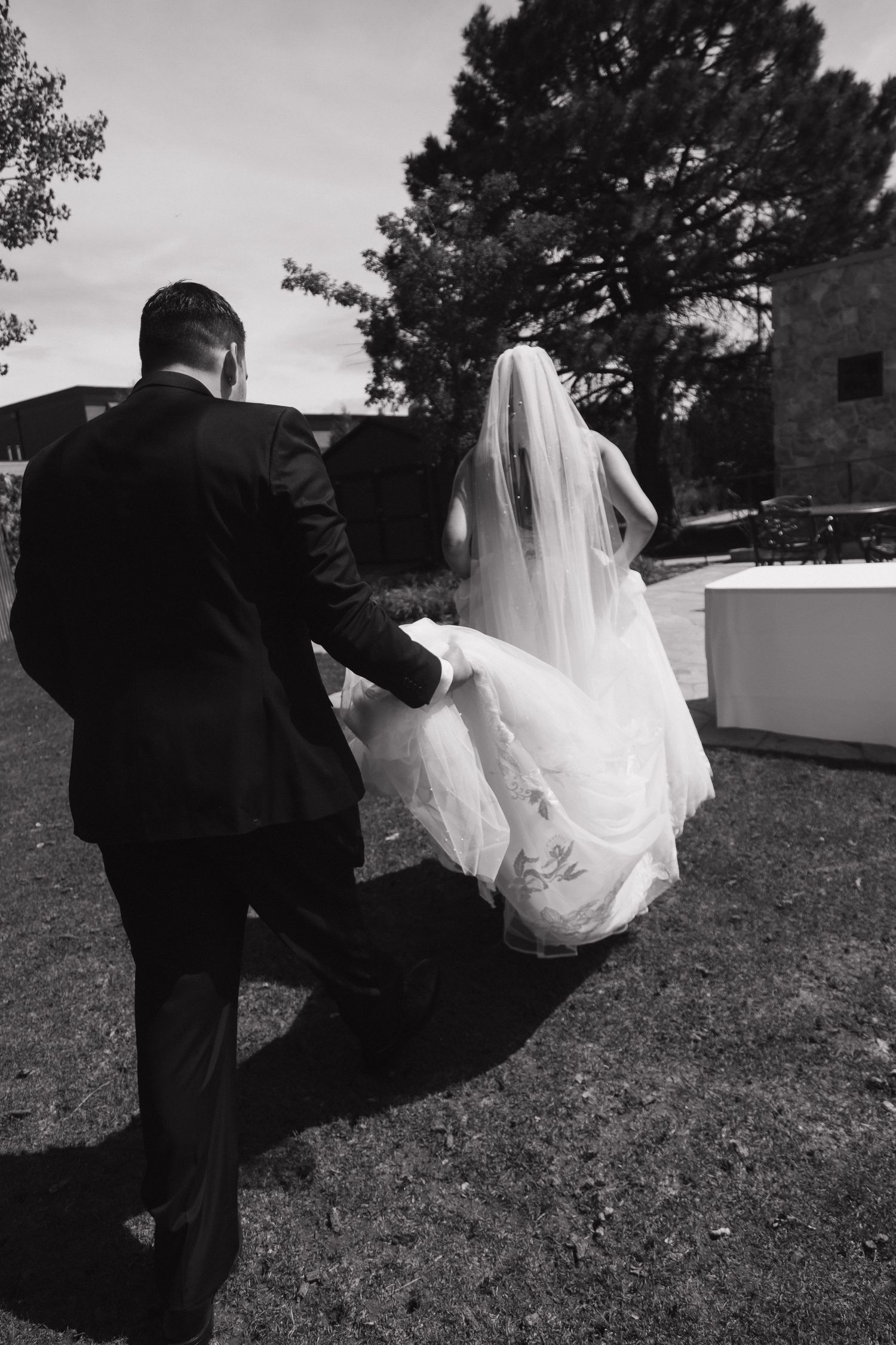 Black and white photo of bride and groom walking together, bride's veil flowing in the breeze.