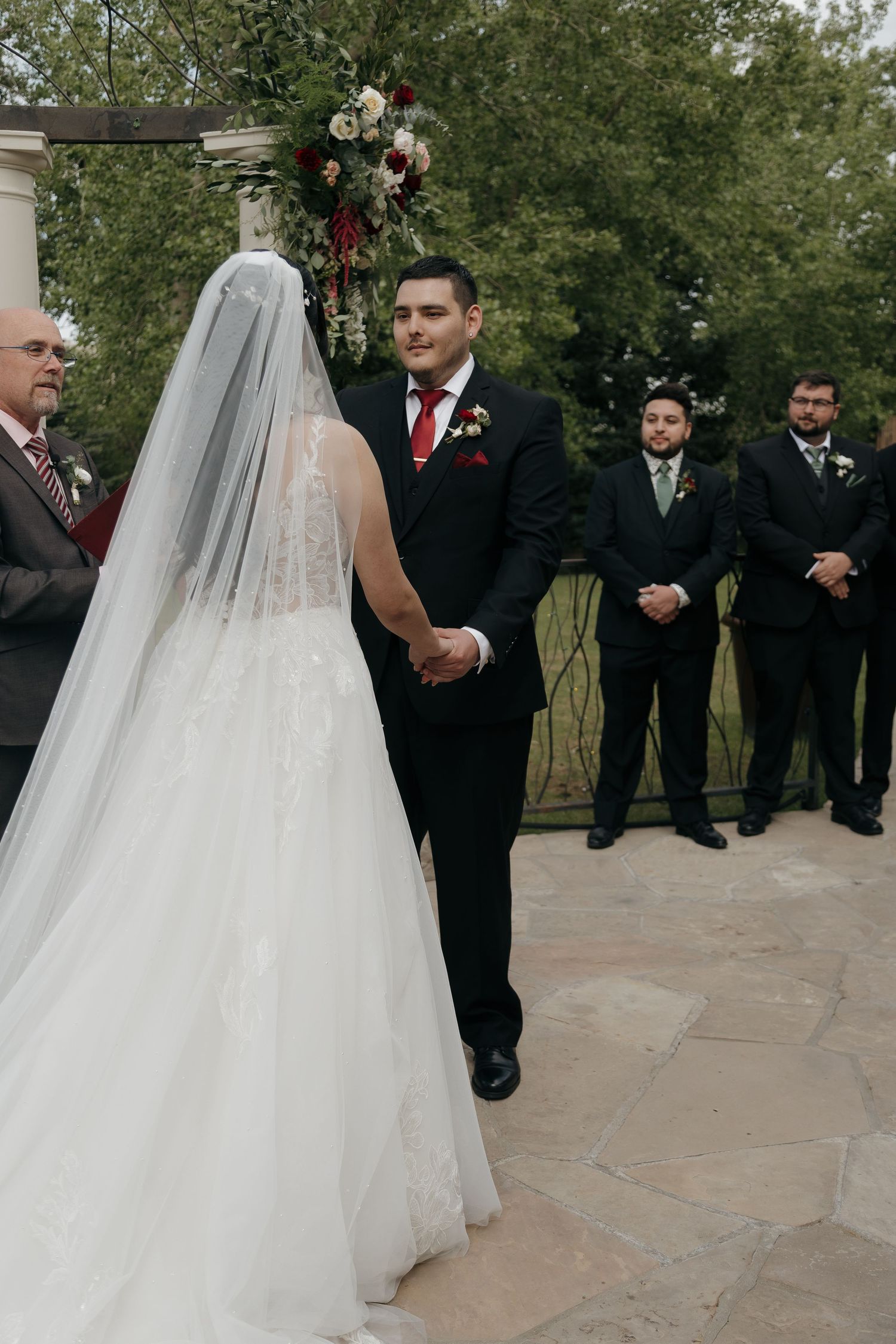 Groom watches bride walk down the aisle at an elegant outdoor wedding ceremony.