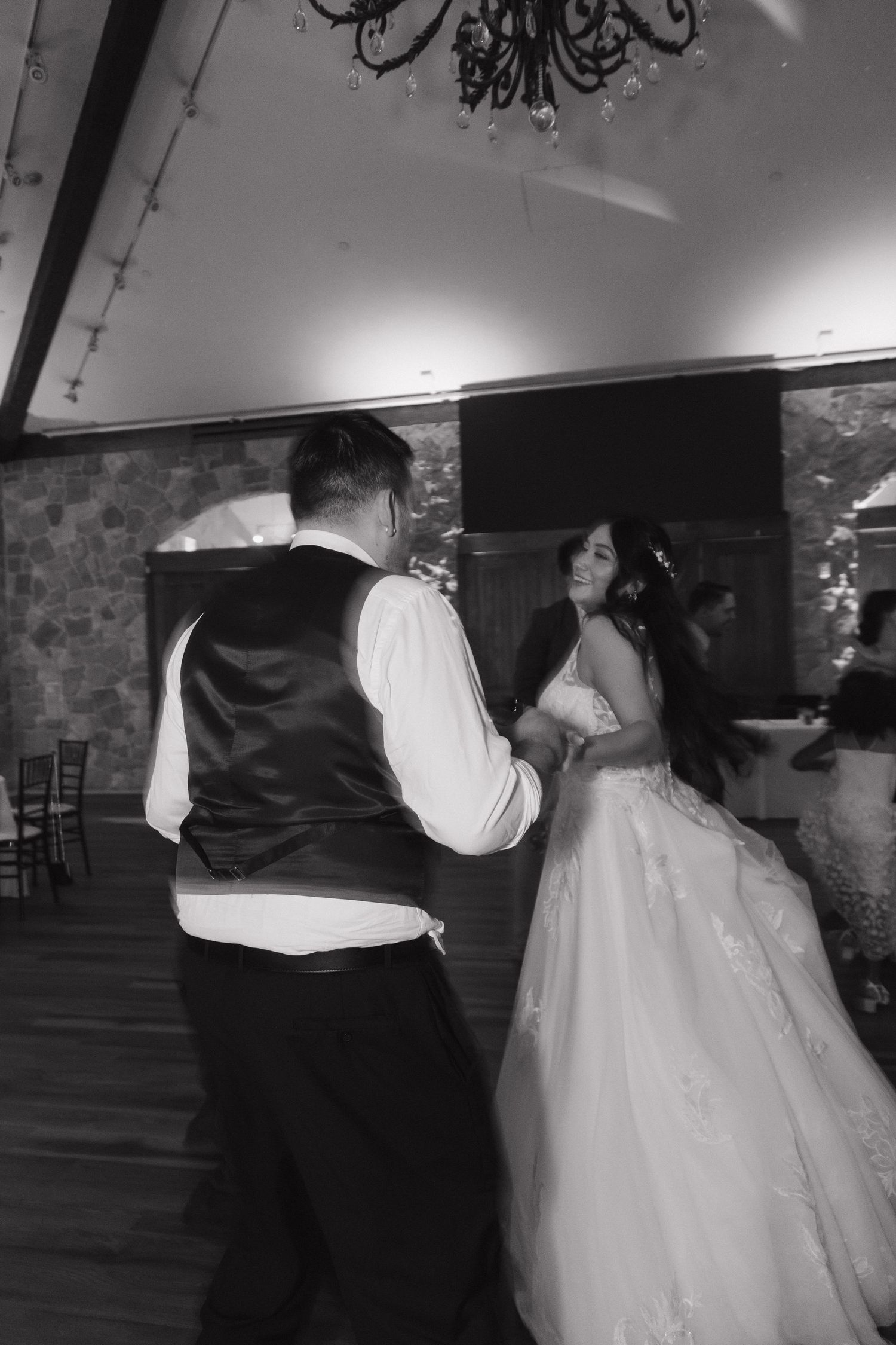 Bride and groom share an intimate dance in a rustic stone ballroom with chandelier lighting.