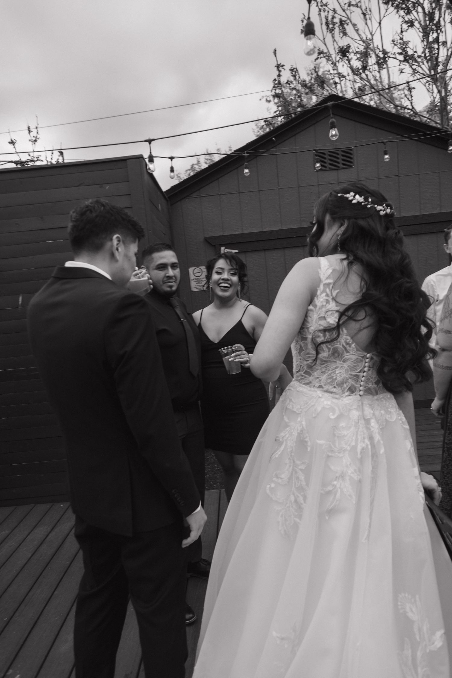 Bride in lace ball gown holds grooms hand while laughing with guests at outdoor wedding reception.