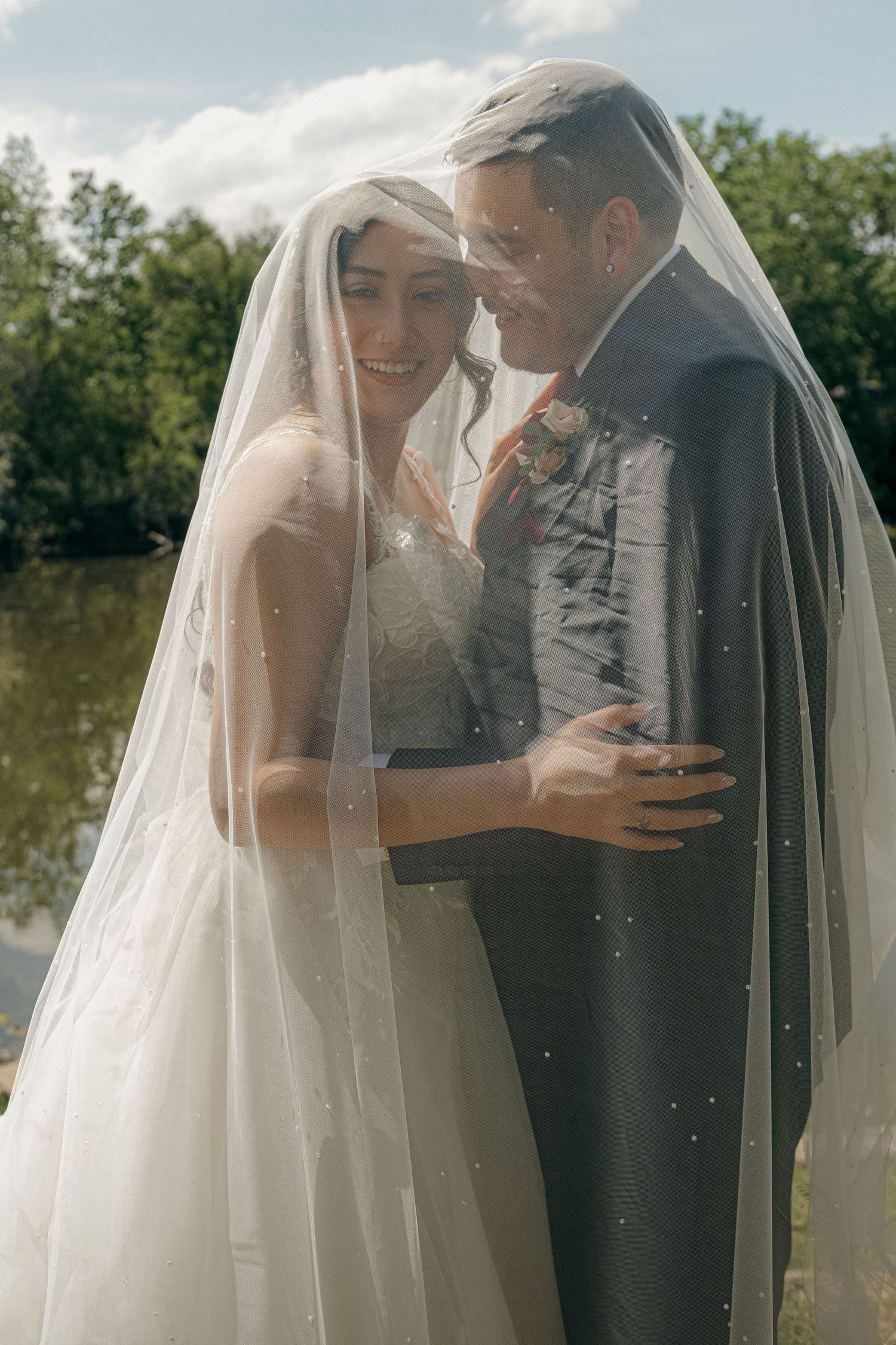 Smiling bride and groom sharing an intimate moment together under a sparkling bridal veil outdoors.