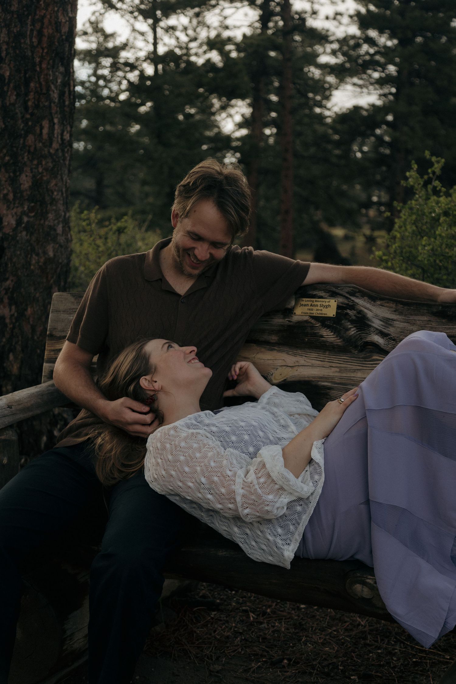 Couple sharing a tender moment on a rustic wooden bench surrounded by pine trees.