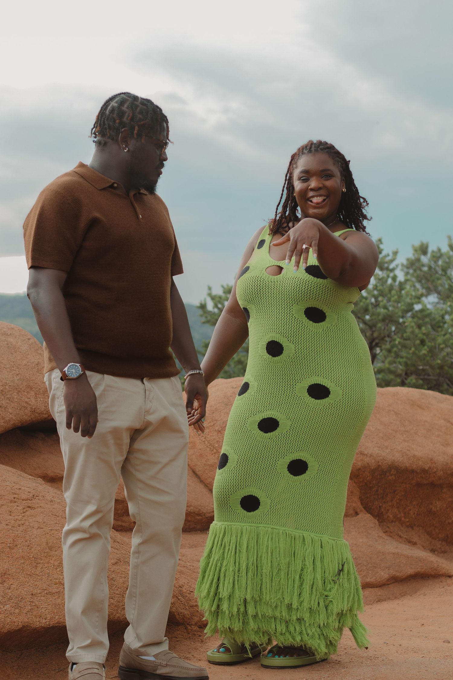 Romantic photoshoot on red rocks featuring a polka dot green dress and brown sweater.