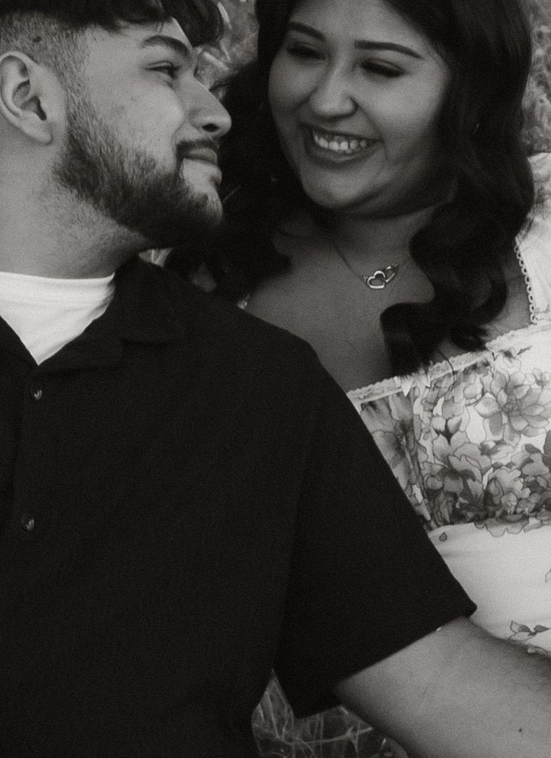 A couple shares an intimate black and white candid moment as they smile together in close profile.