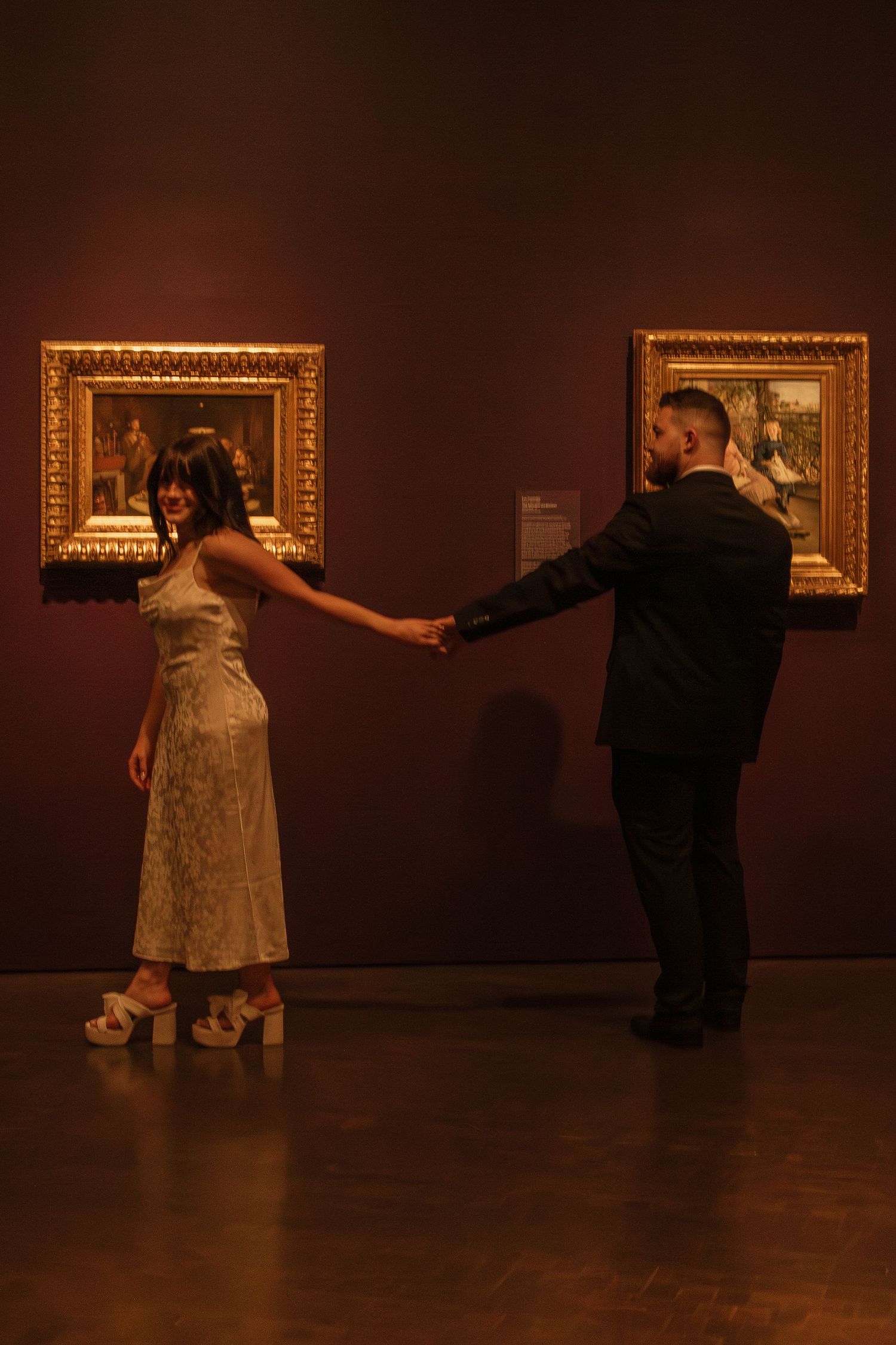 A couple dances in a dimly lit art gallery with ornate gold frames on the walls.