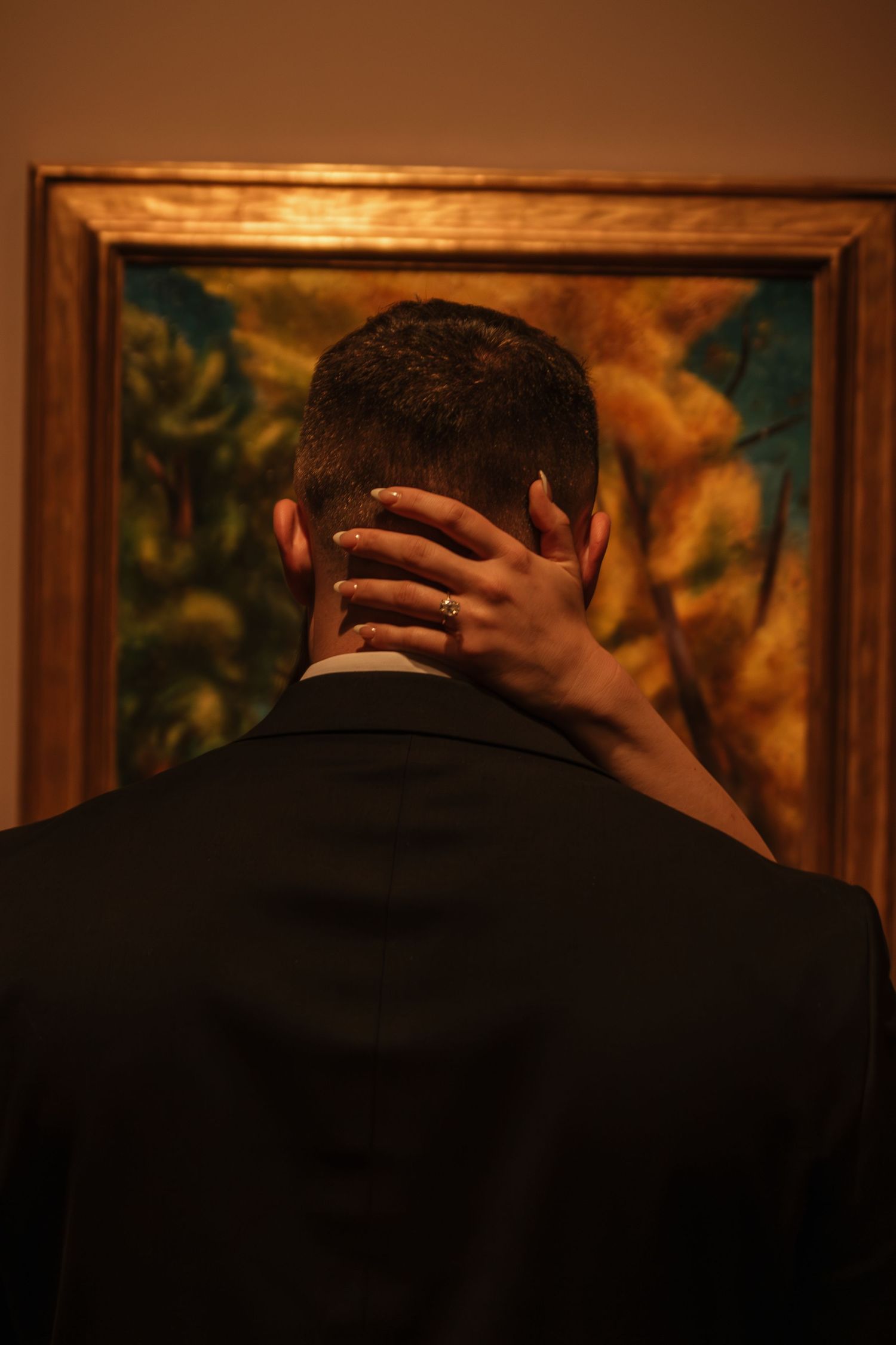 Close embrace against backdrop of vibrant artwork in golden frames.