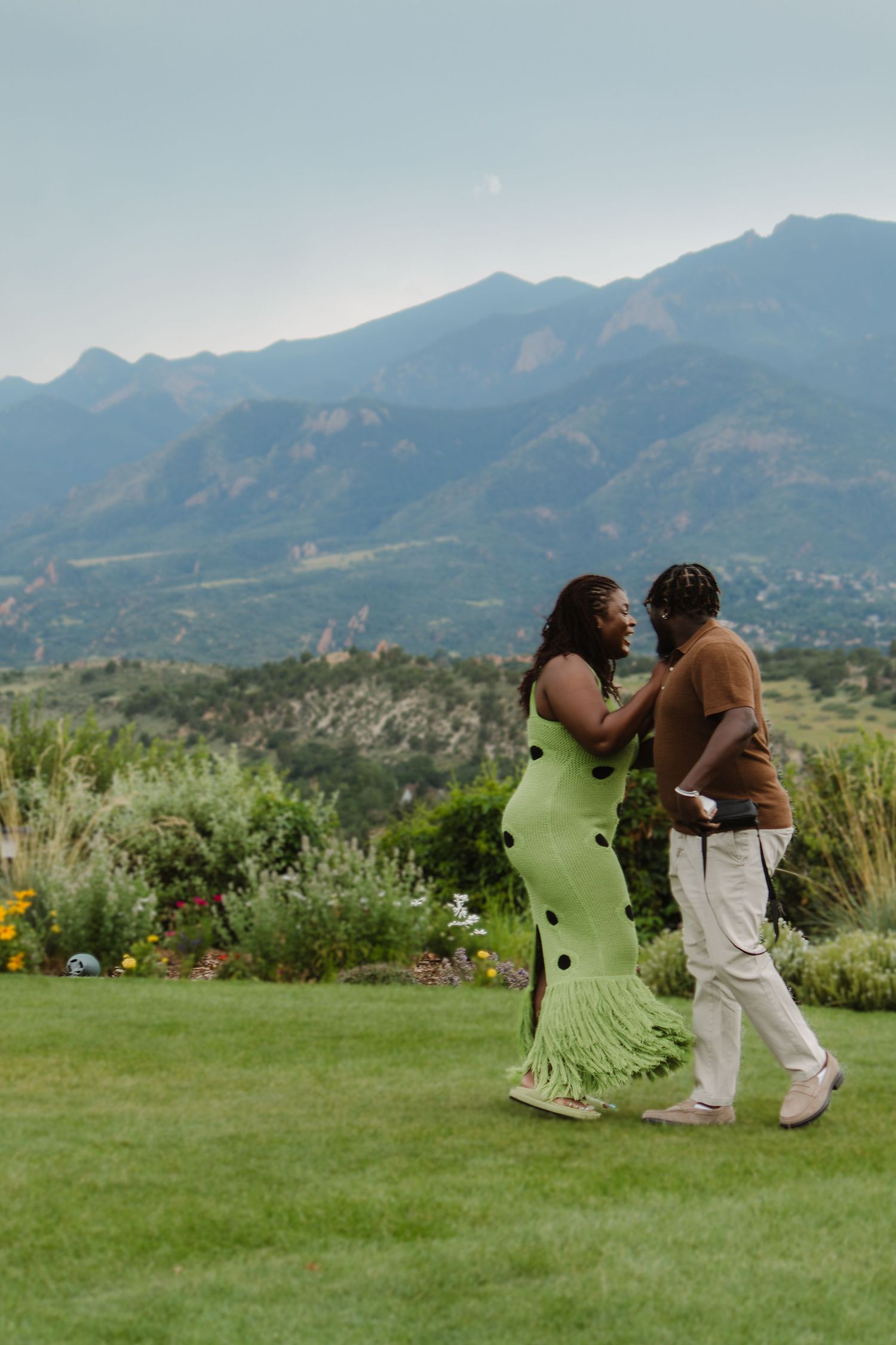 Two people dance playfully on a grassy lawn with scenic mountain views in the background.
