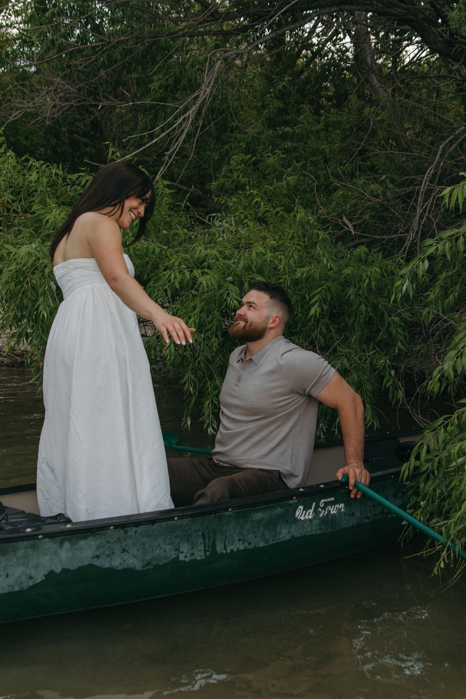 A couple shares a relaxed moment together in a green canoe near lush foliage.