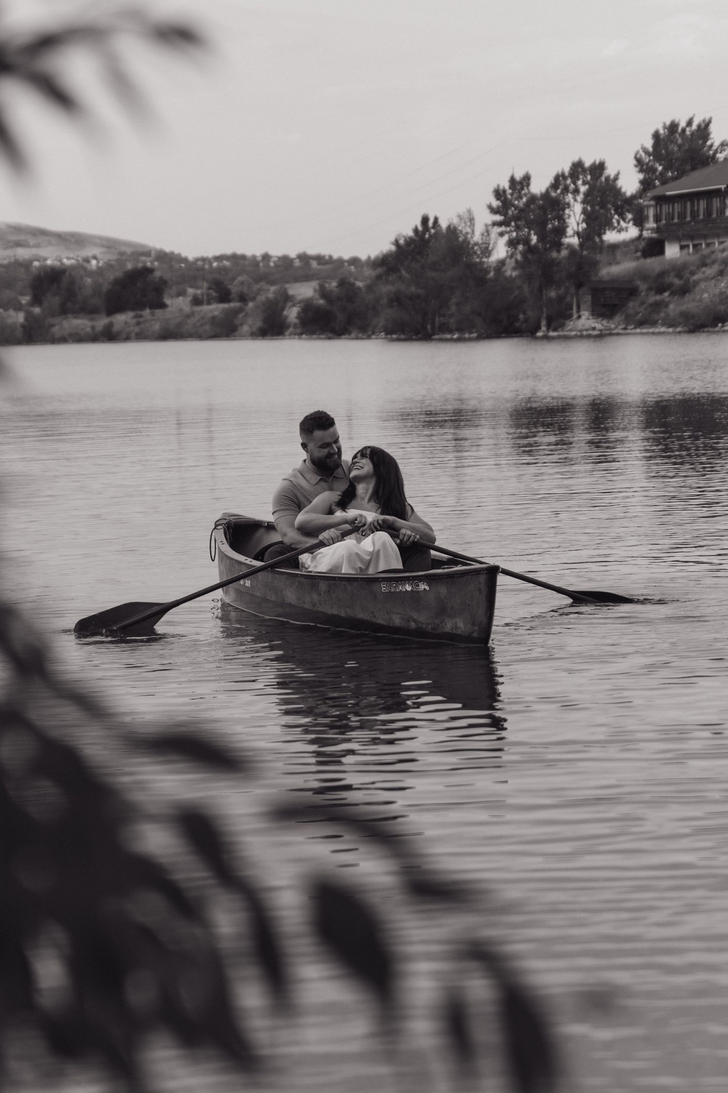 A rowboat glides across a peaceful lake surrounded by mountains and trees.