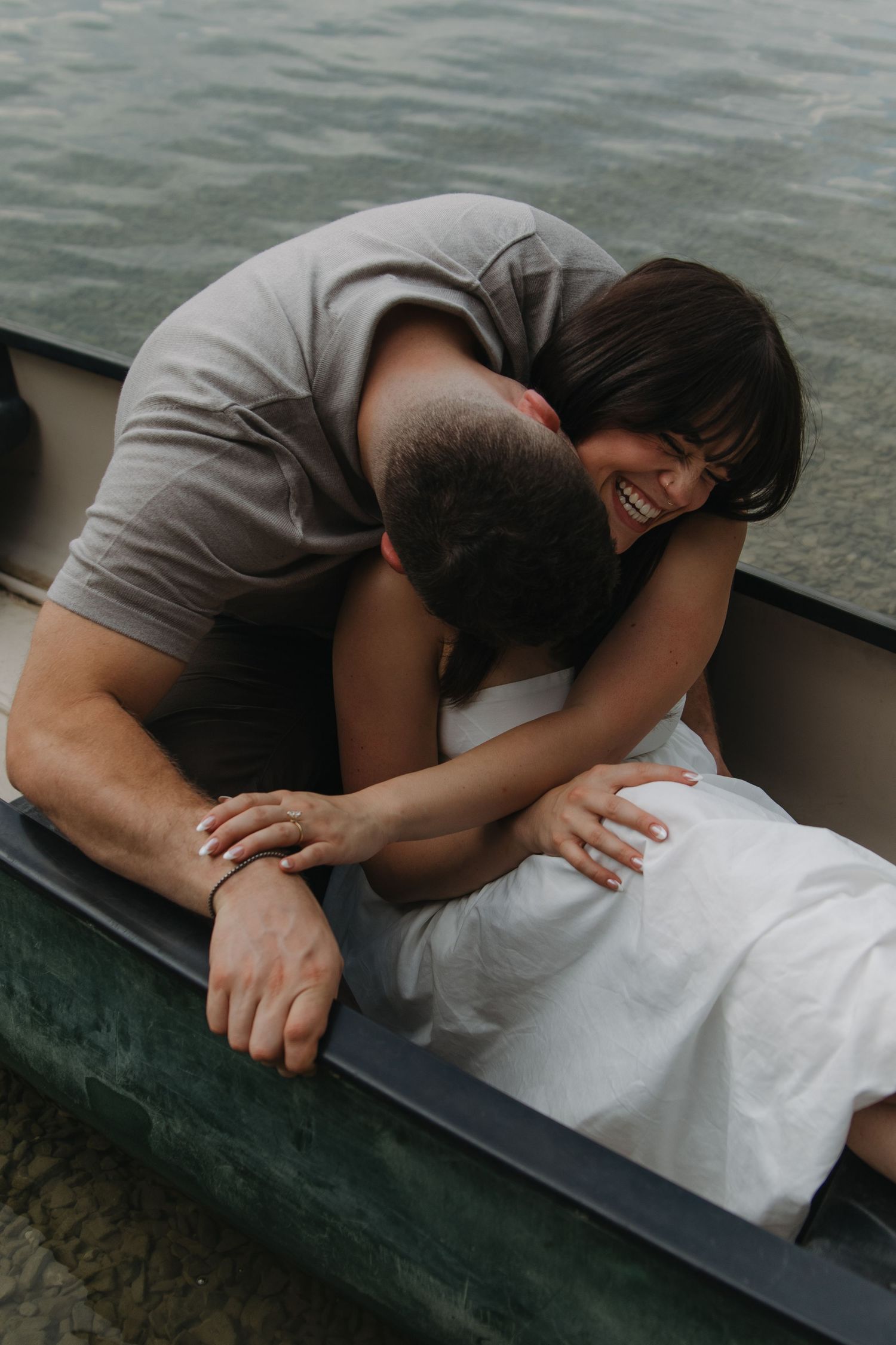 Two people sharing an intimate moment in a dark green canoe on calm waters.