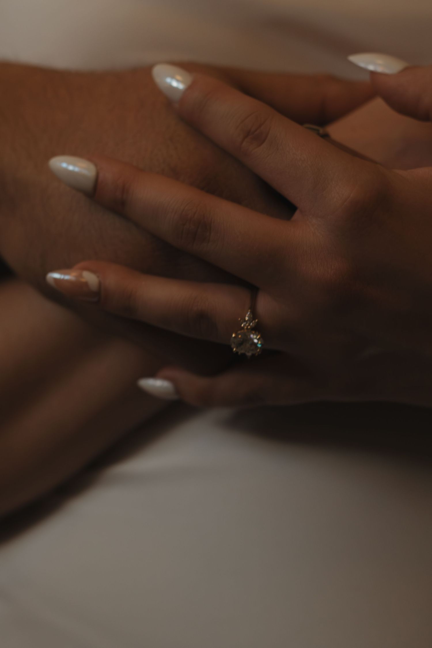 Close up of hands with white manicured nails and a sparkling engagement ring.
