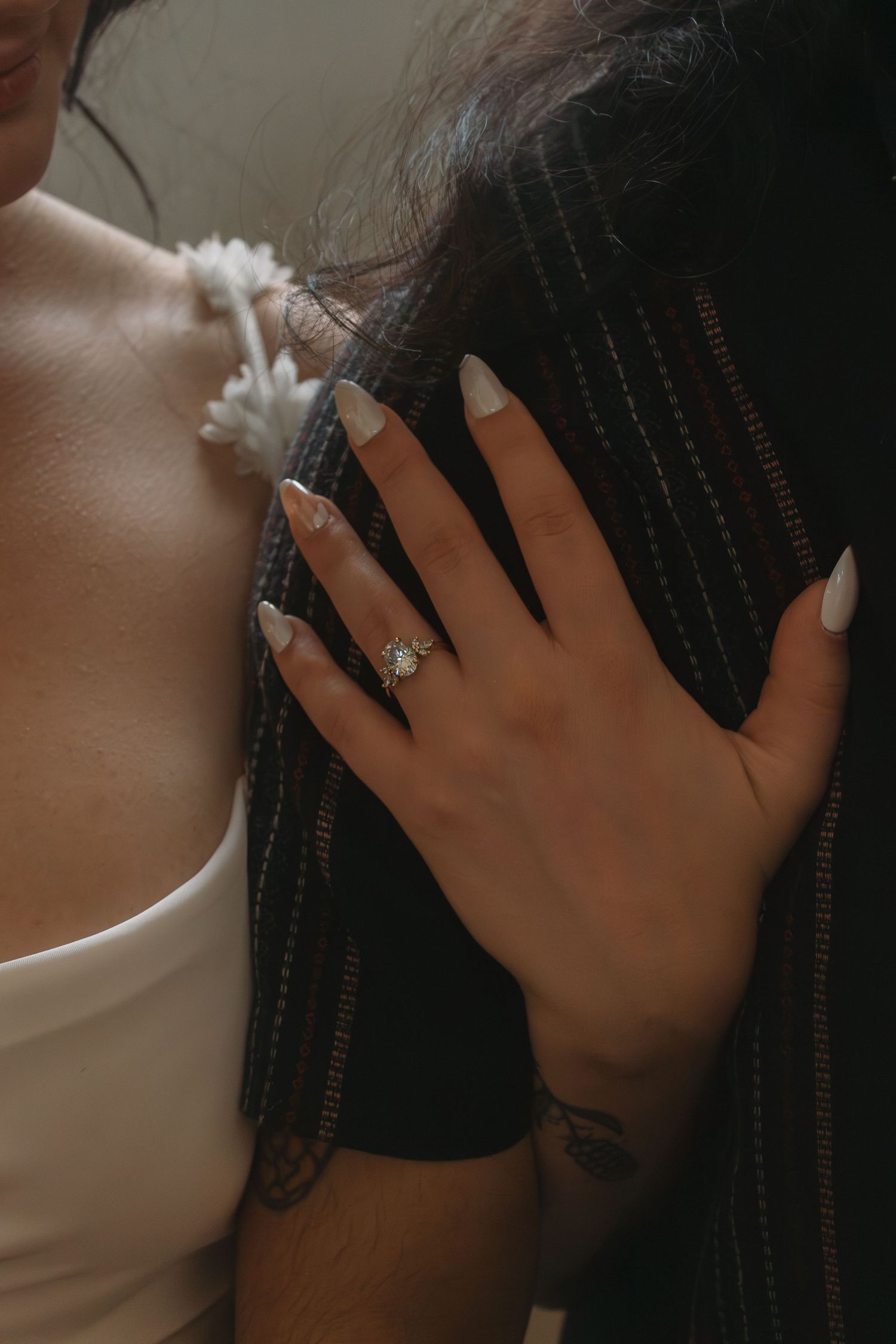Close-up of a hand with painted nails and engagement ring resting against dark fabric.