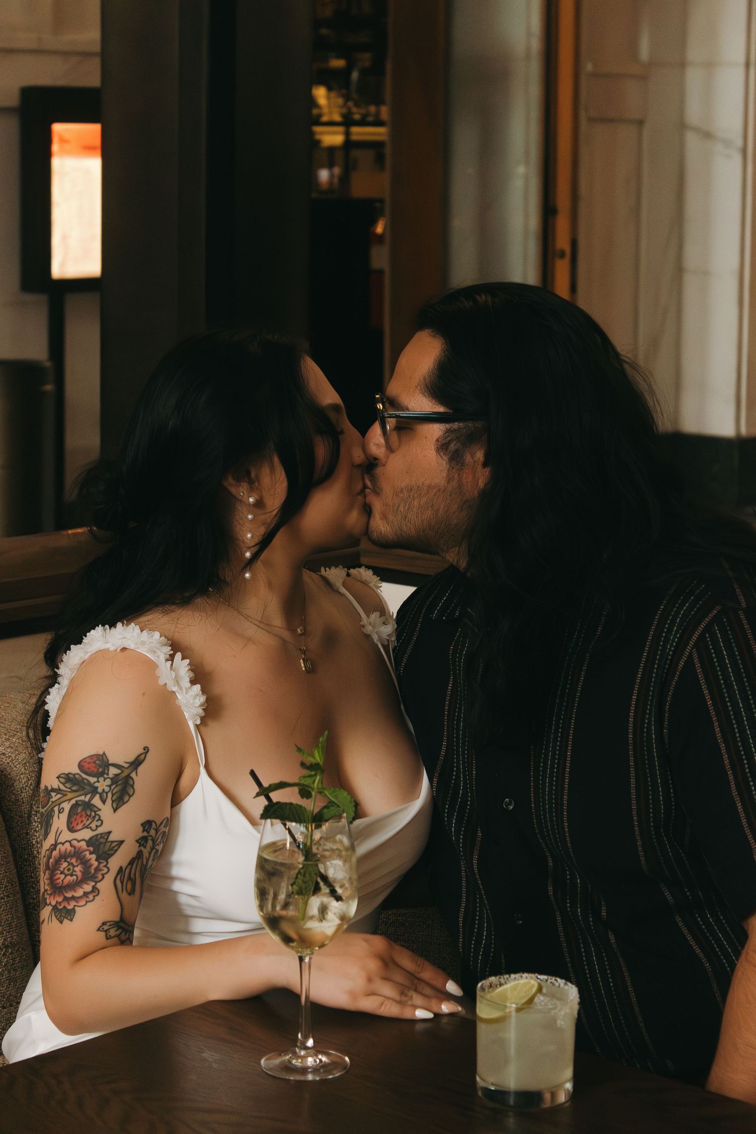 A dimly lit bar scene shows tattoo art and cocktail glasses in an intimate setting with dark decor.