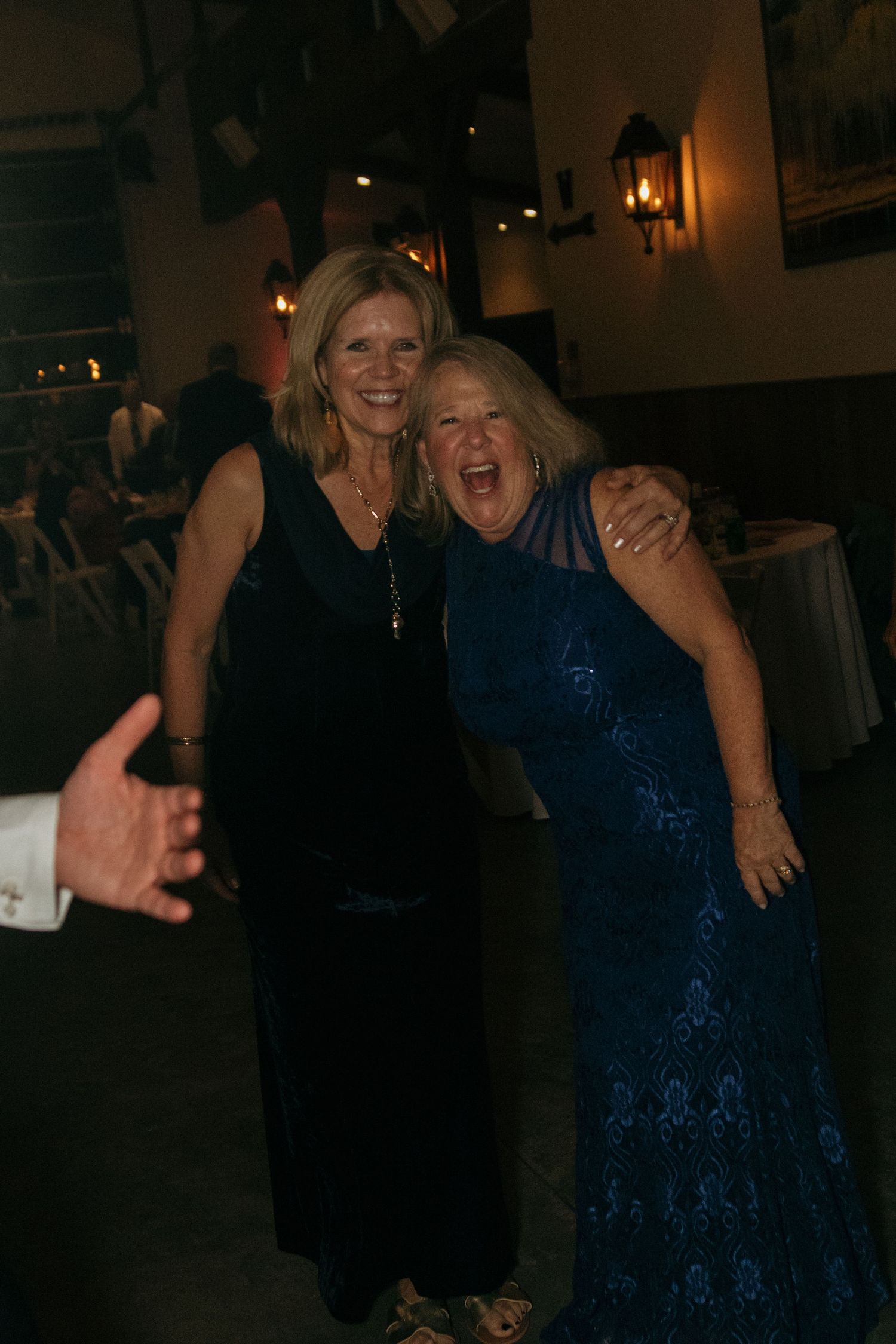 Two people laughing and dancing together at a dimly lit party venue wearing formal attire.