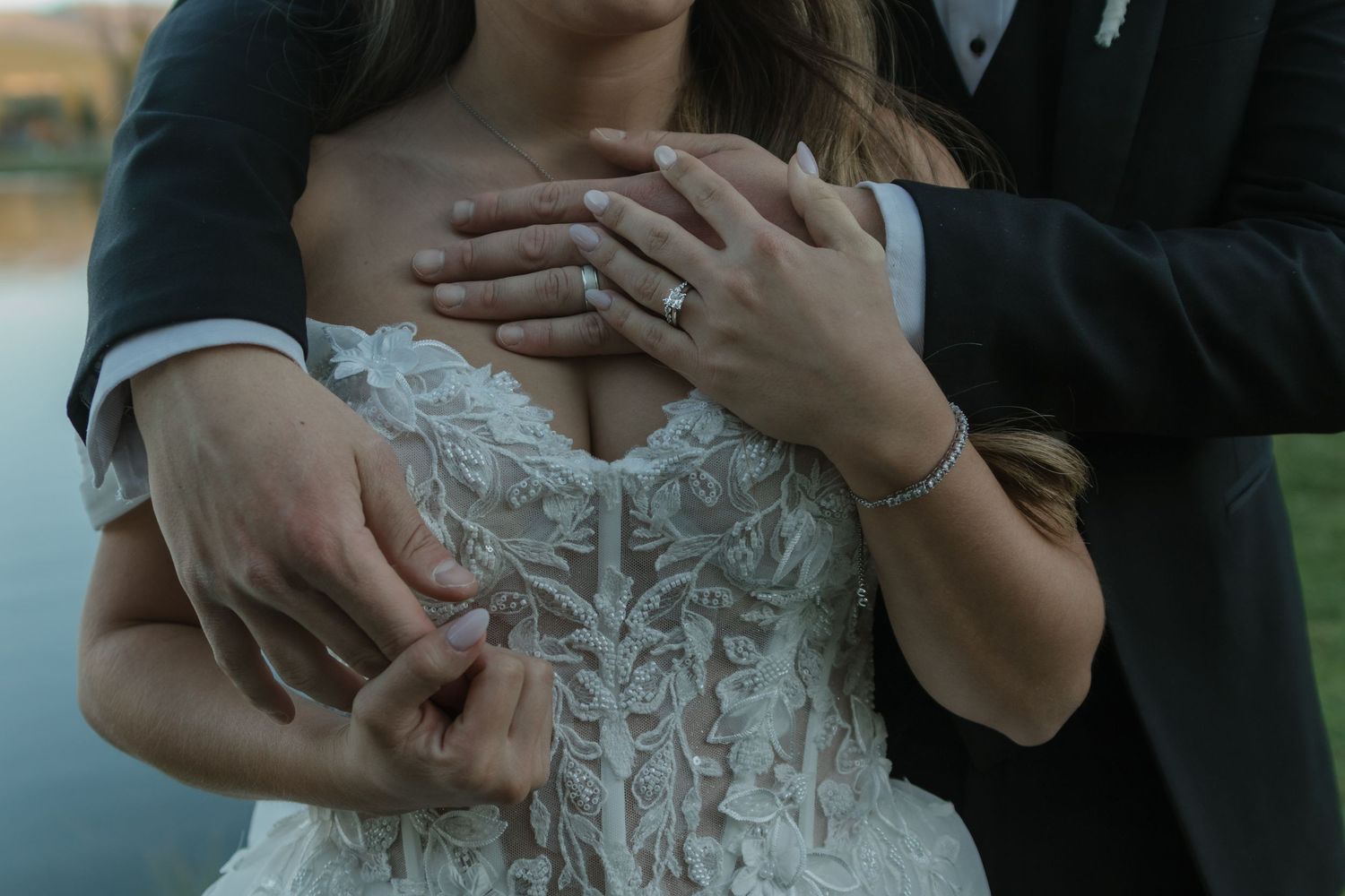 Close-up shot of bride and groom's hands showing wedding rings against formal attire.