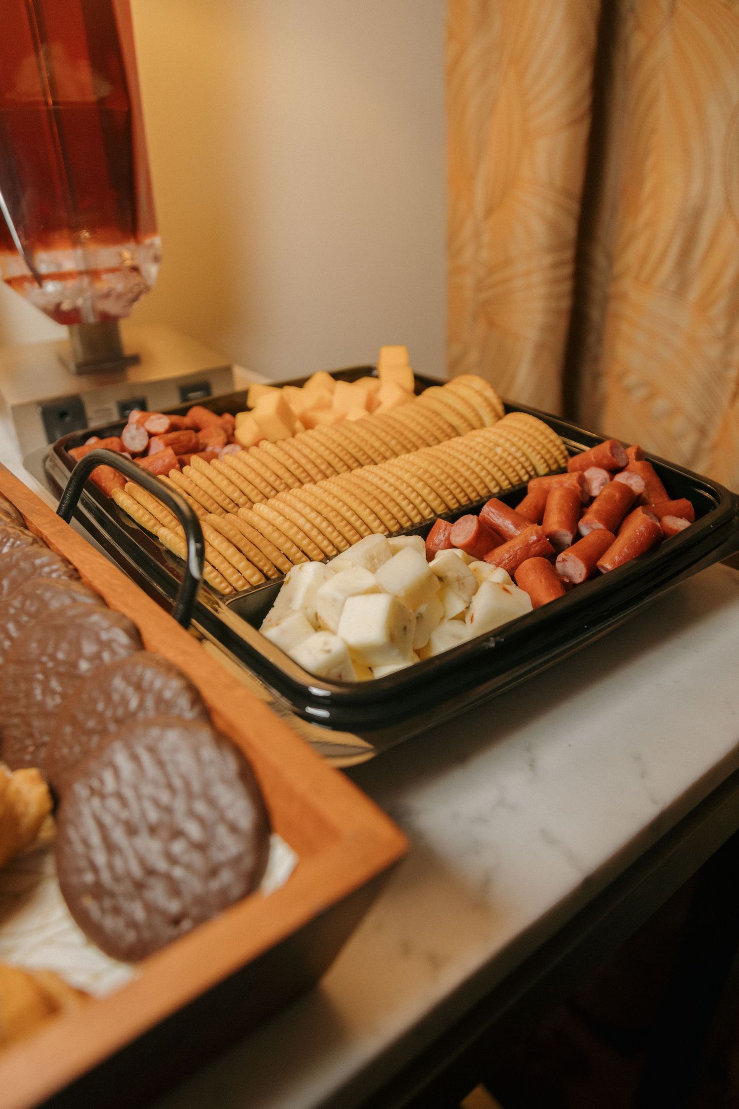 A charcuterie tray with crackers, mini sausages, cheese cubes, and snacks on a marble table.