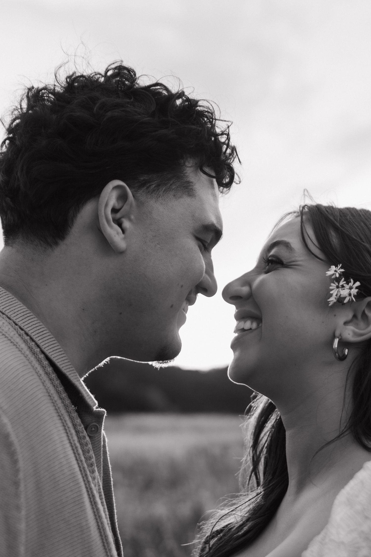 Black and white close-up of couple smiling face to face outdoors in a romantic moment.