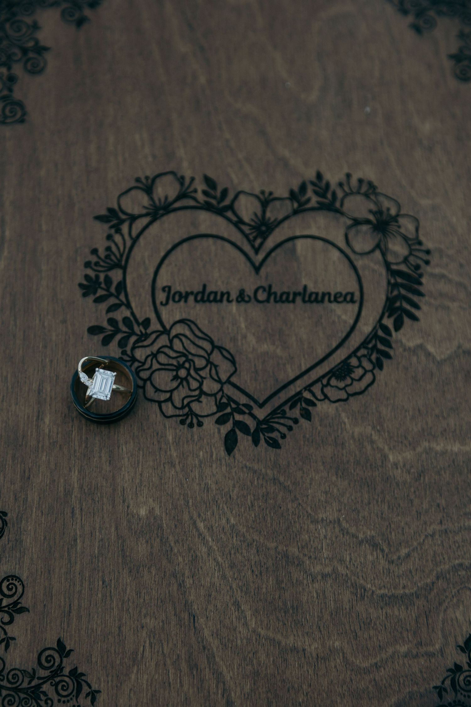 Engagement ring on wooden surface engraved with Jordan and Charlanea heart design.