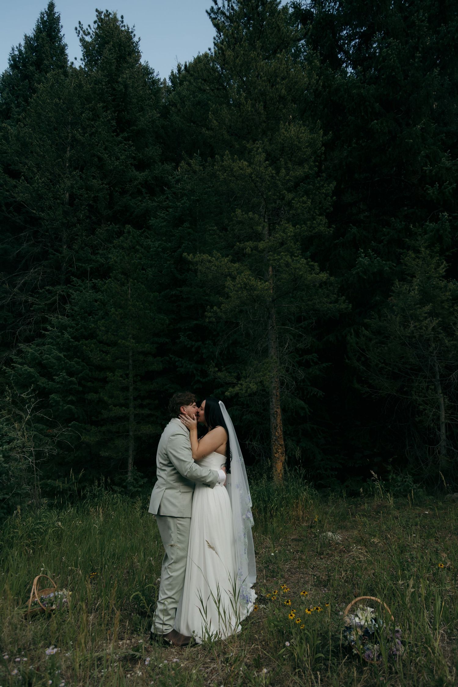 Bride and groom share a romantic kiss in a lush forest meadow during their outdoor wedding ceremony.
