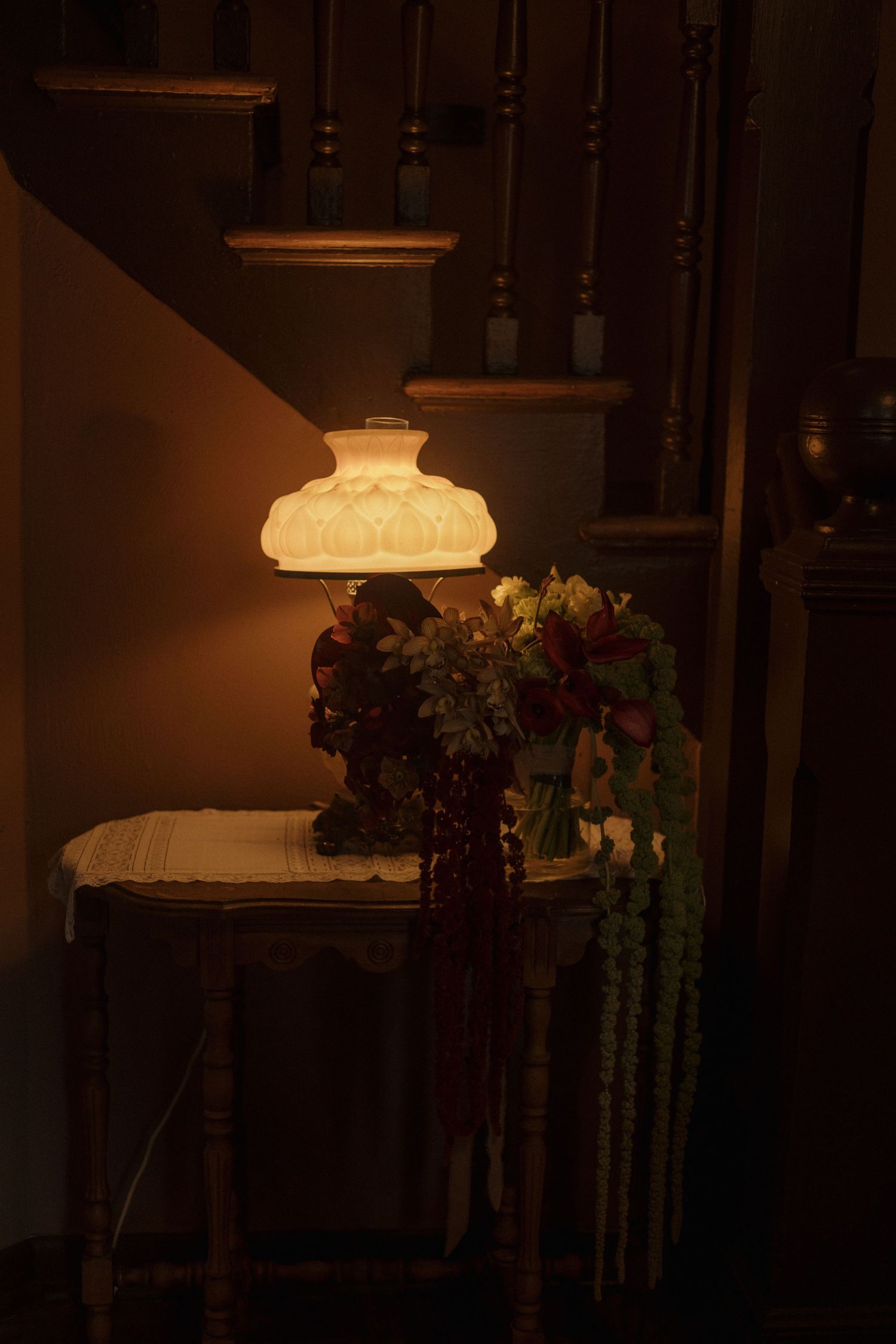 A vintage table lamp with a frosted glass shade casts a warm glow near a wooden staircase.