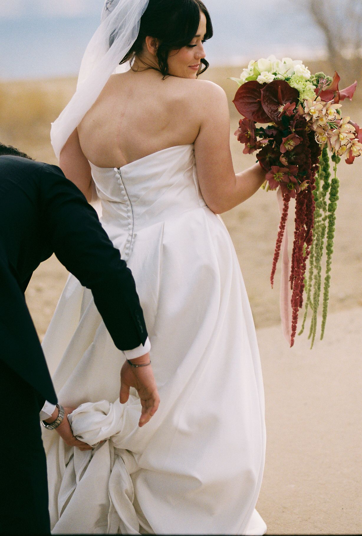 Romantic outdoor wedding photo with flowing white dress and trailing bouquet.