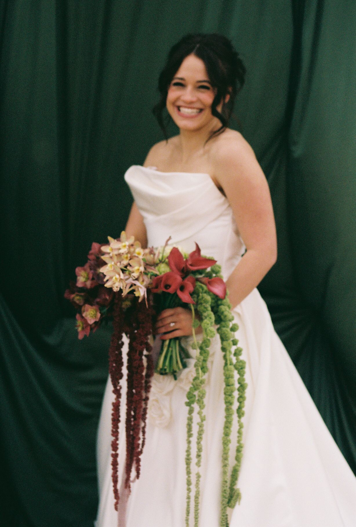 Elegant bridal portrait with cascading autumn-colored bouquet against emerald backdrop.
