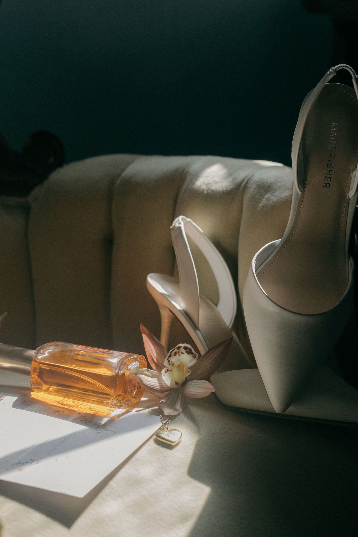 White bridal shoes and perfume bottle catching sunlight on a windowsill.