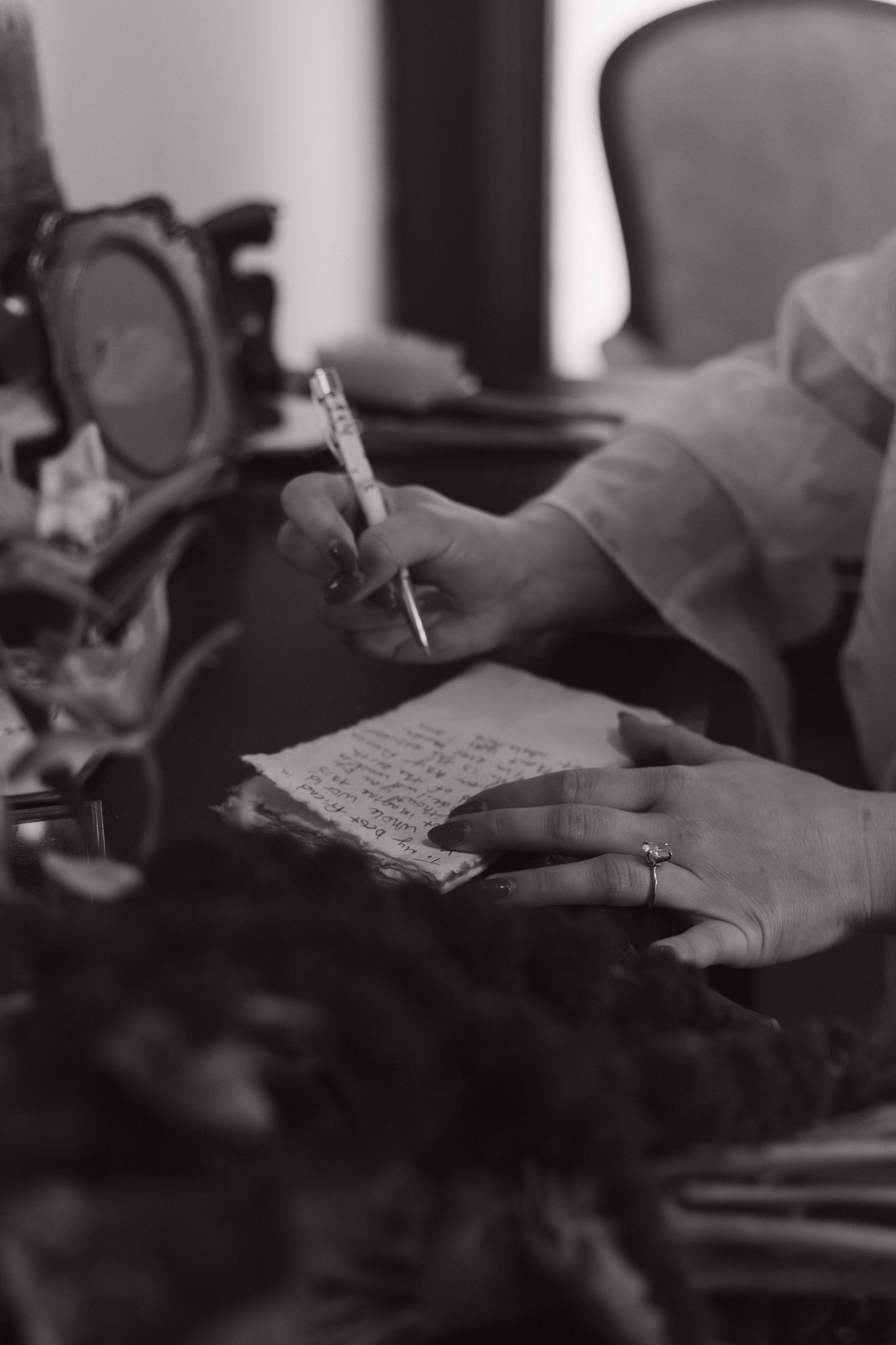 Black and white close-up of hands writing wedding vows on paper.