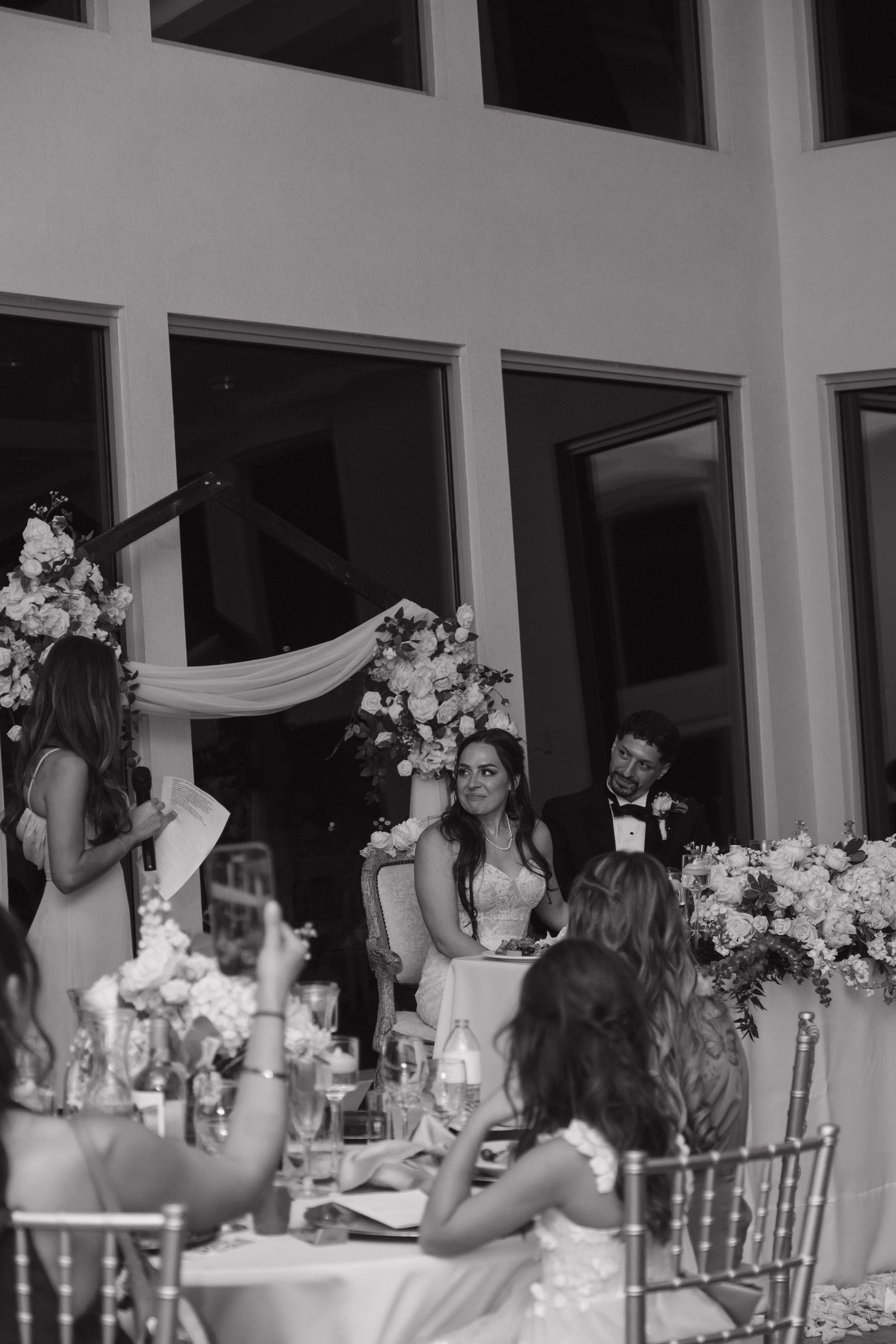 Bride and groom at sweetheart table with floral arrangements during black and white wedding reception.