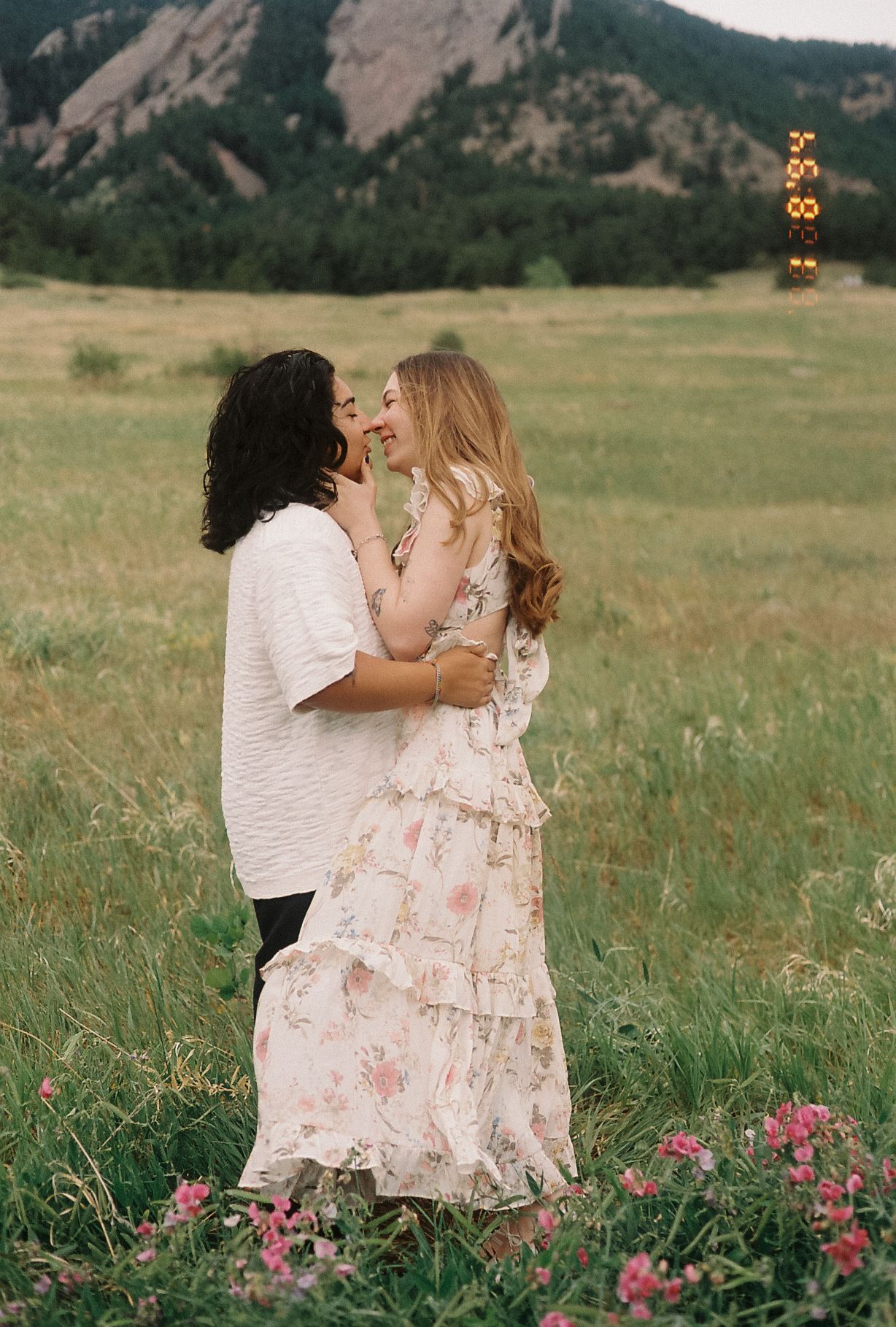 Couple embracing and smiling in a green meadow with Rocky Mountain flatirons in the background.