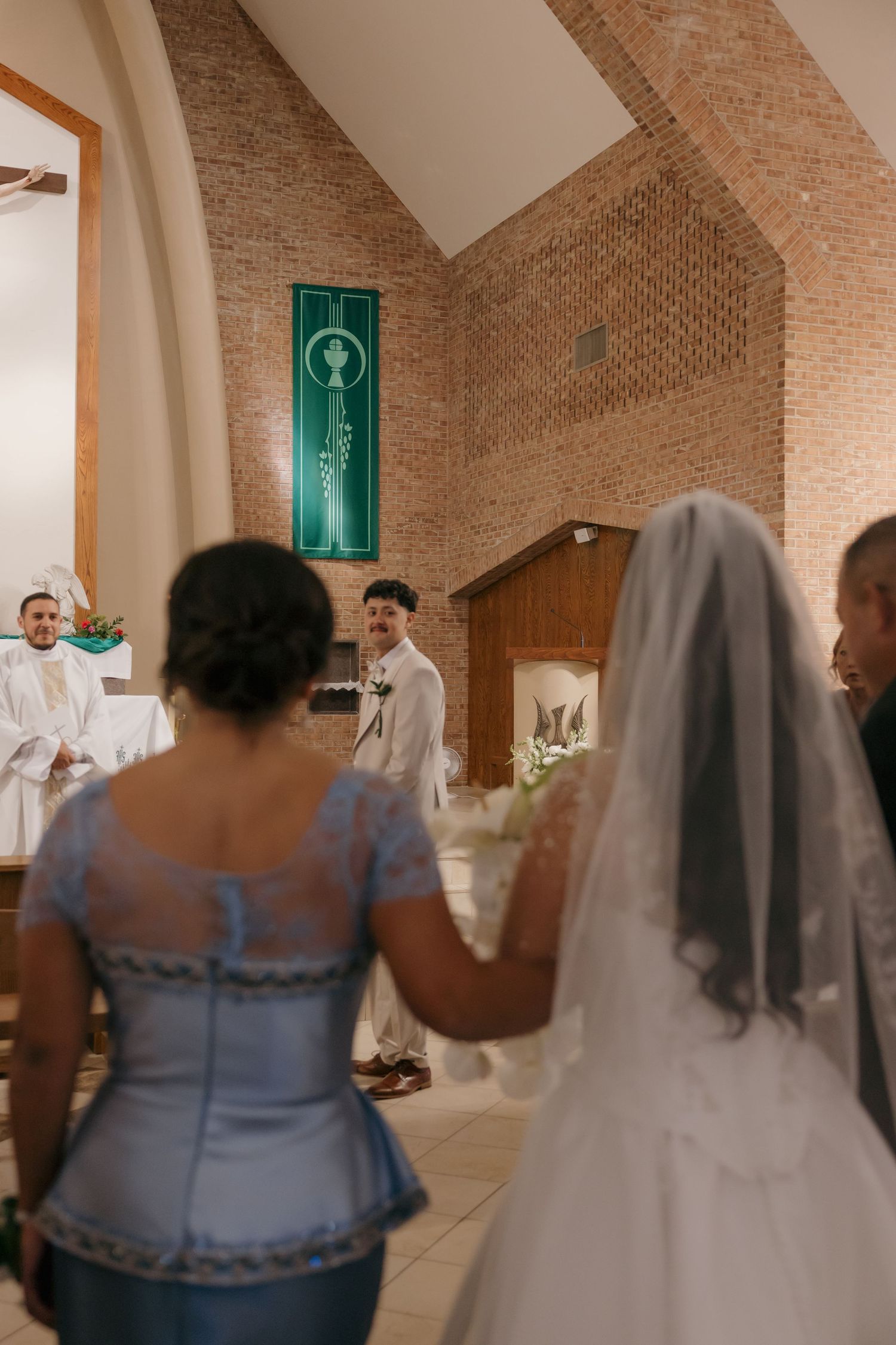 Bride walking down church aisle toward smiling groom at altar during Catholic wedding ceremony.
