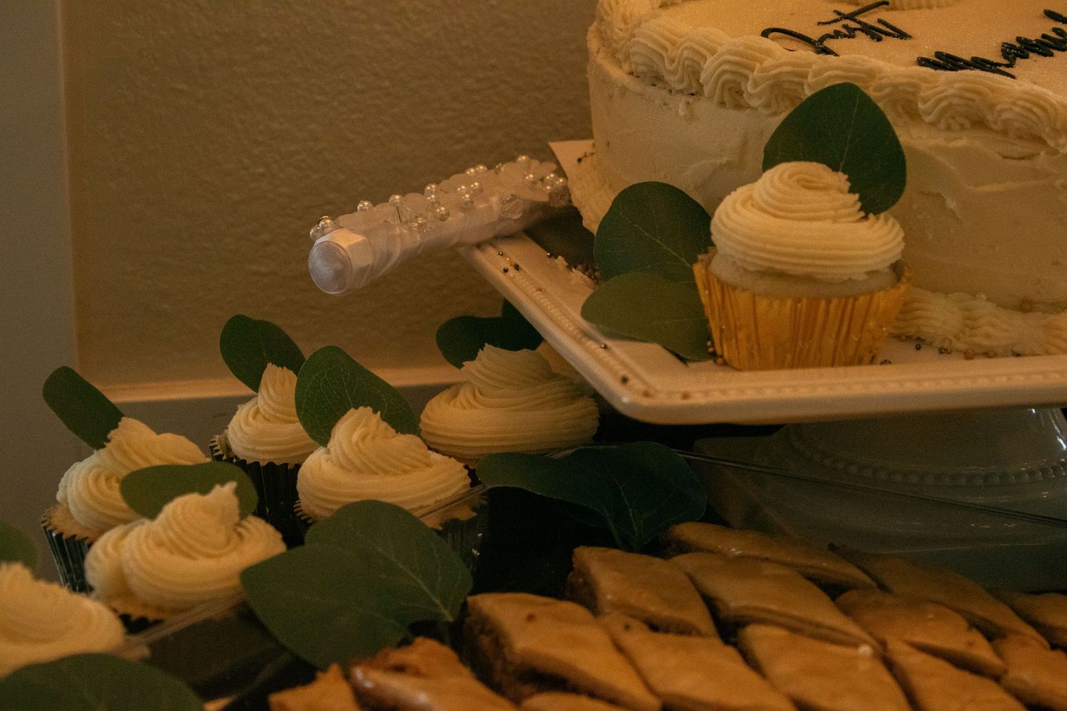 Wedding dessert table with decorated cupcakes garnished with green leaves on a white serving tray.