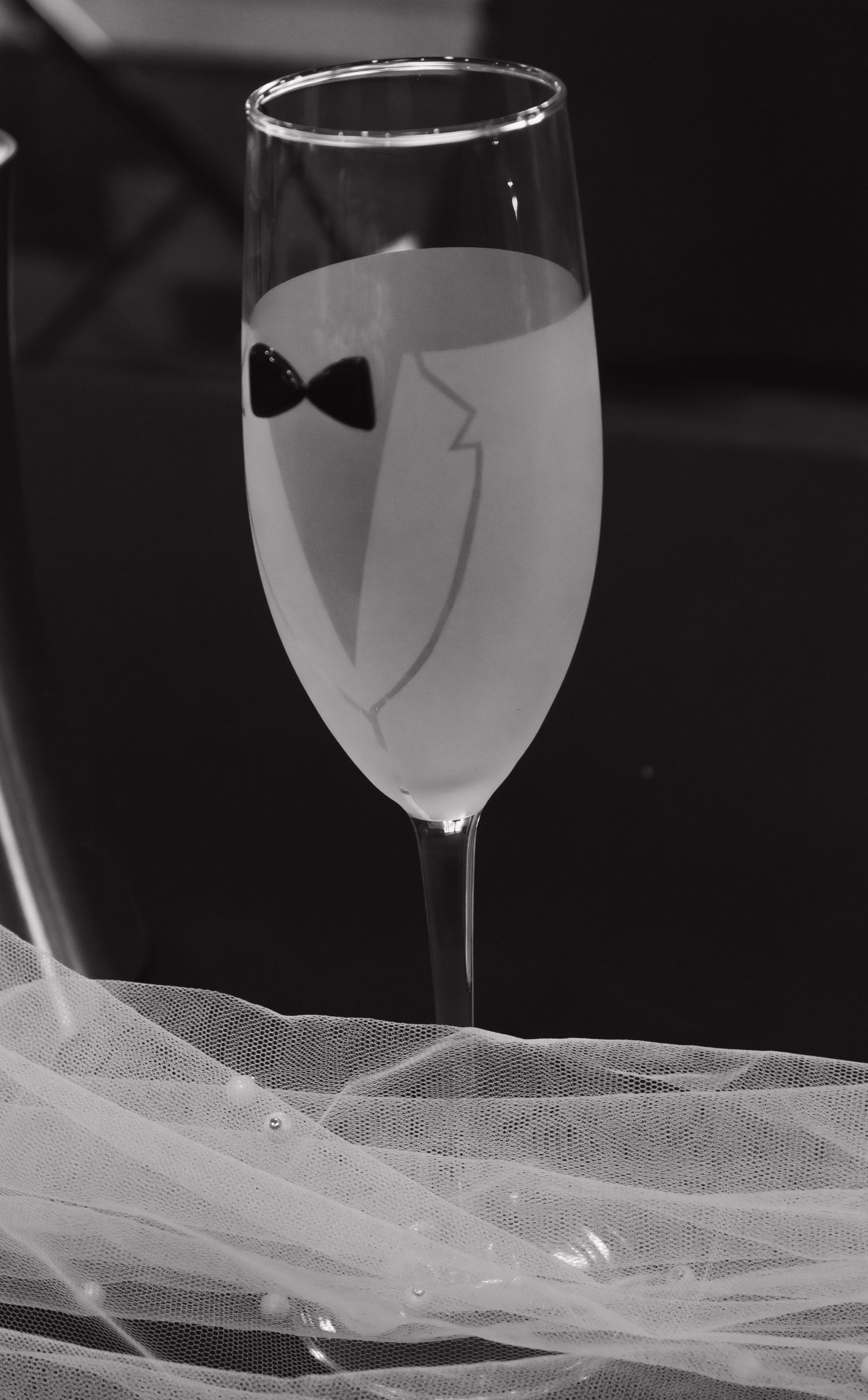 Artistic shot of champagne glass with tuxedo design against flowing white fabric.