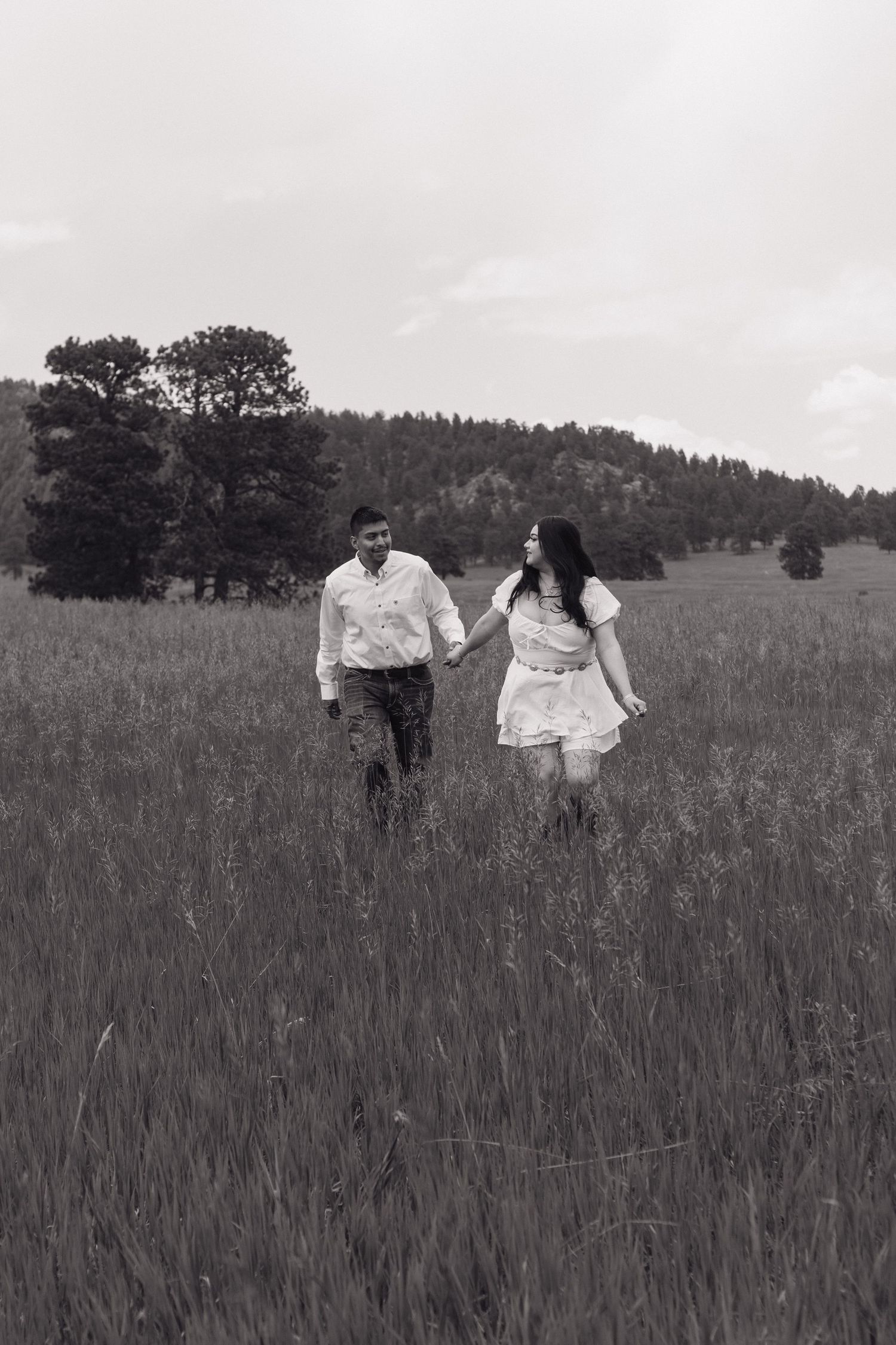 Black and white photograph capturing a playful moment between a couple in a meadow.