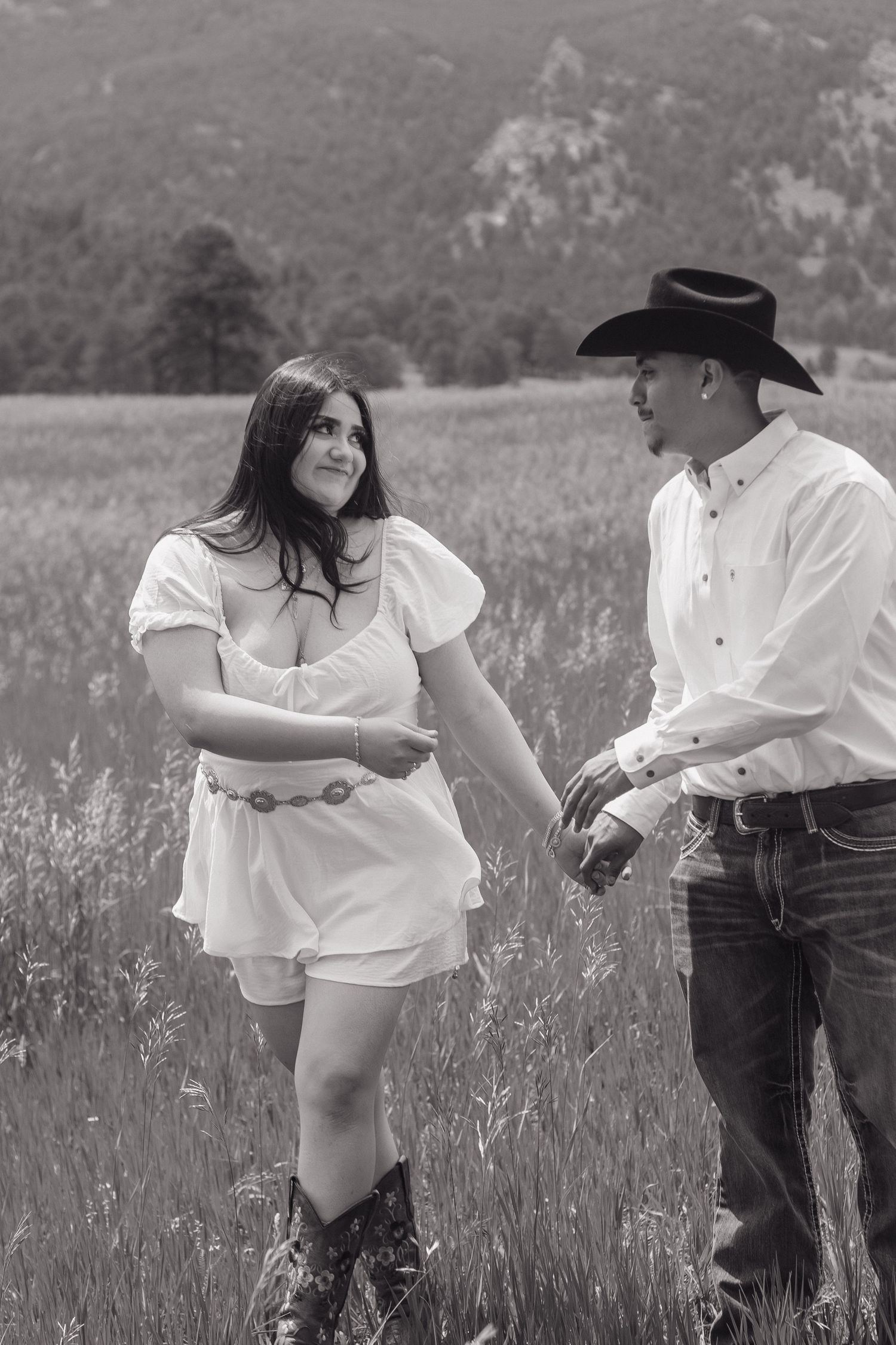 Black and white portrait of couple in western wear standing together in mountain field.