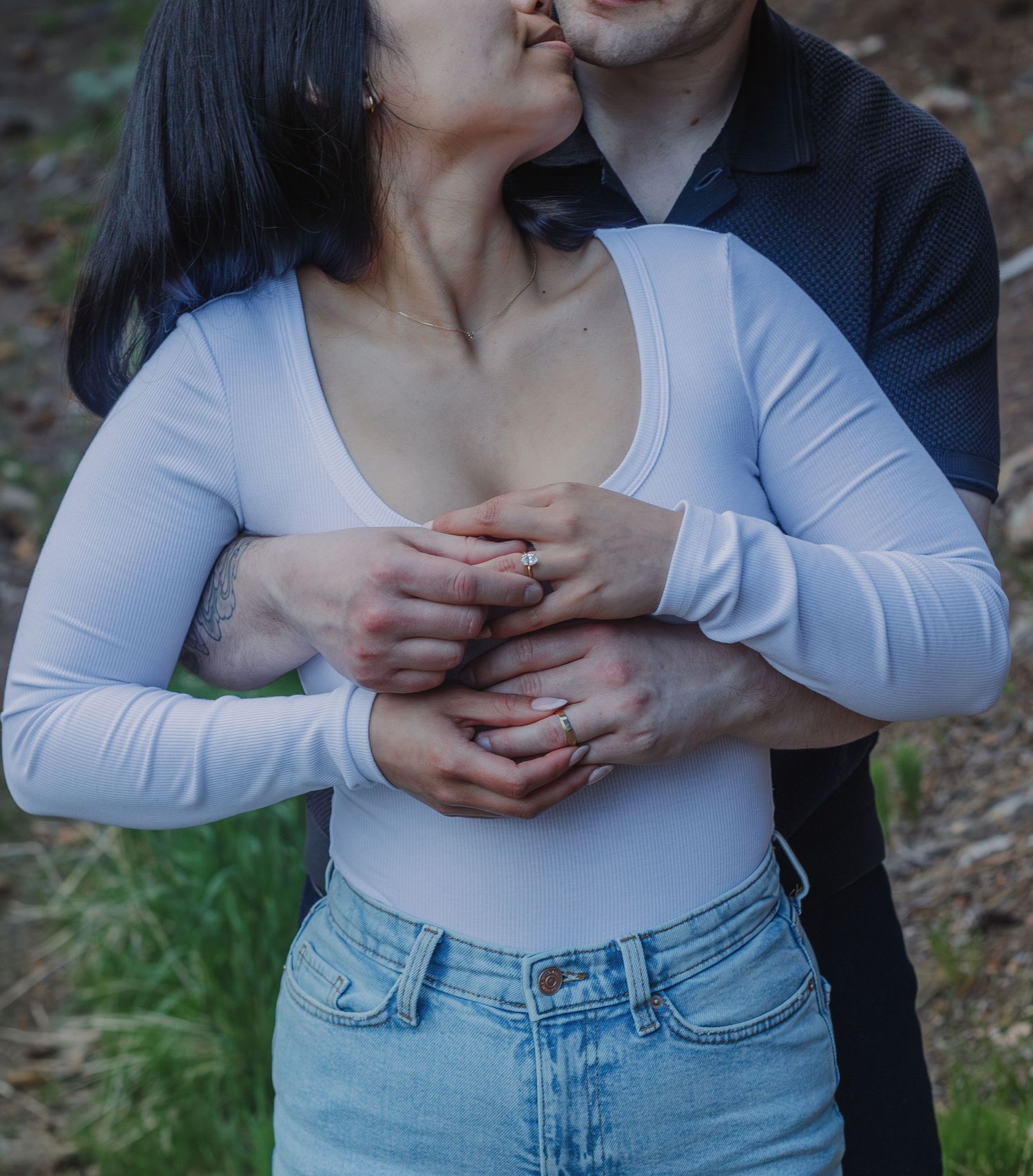 Intimate moment captured showing hands with wedding rings and a white top with blue jeans.