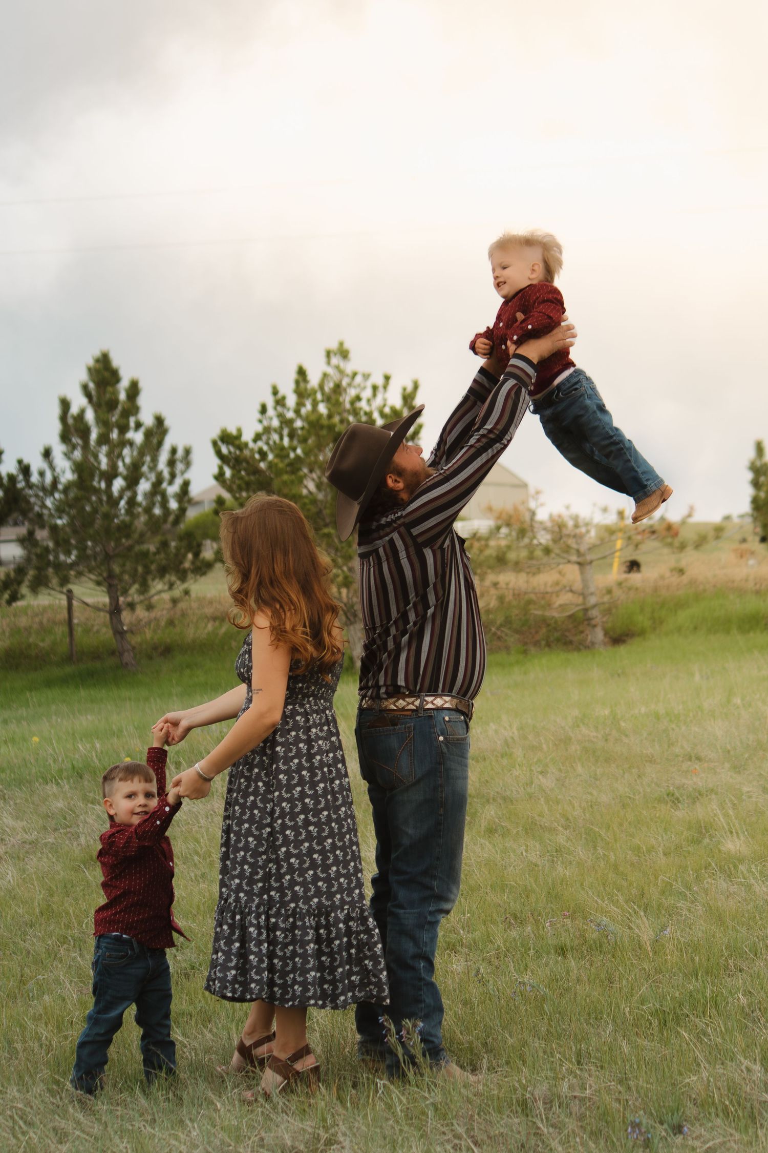 Playful family moment captured in a field as parents lift their children during sunset.